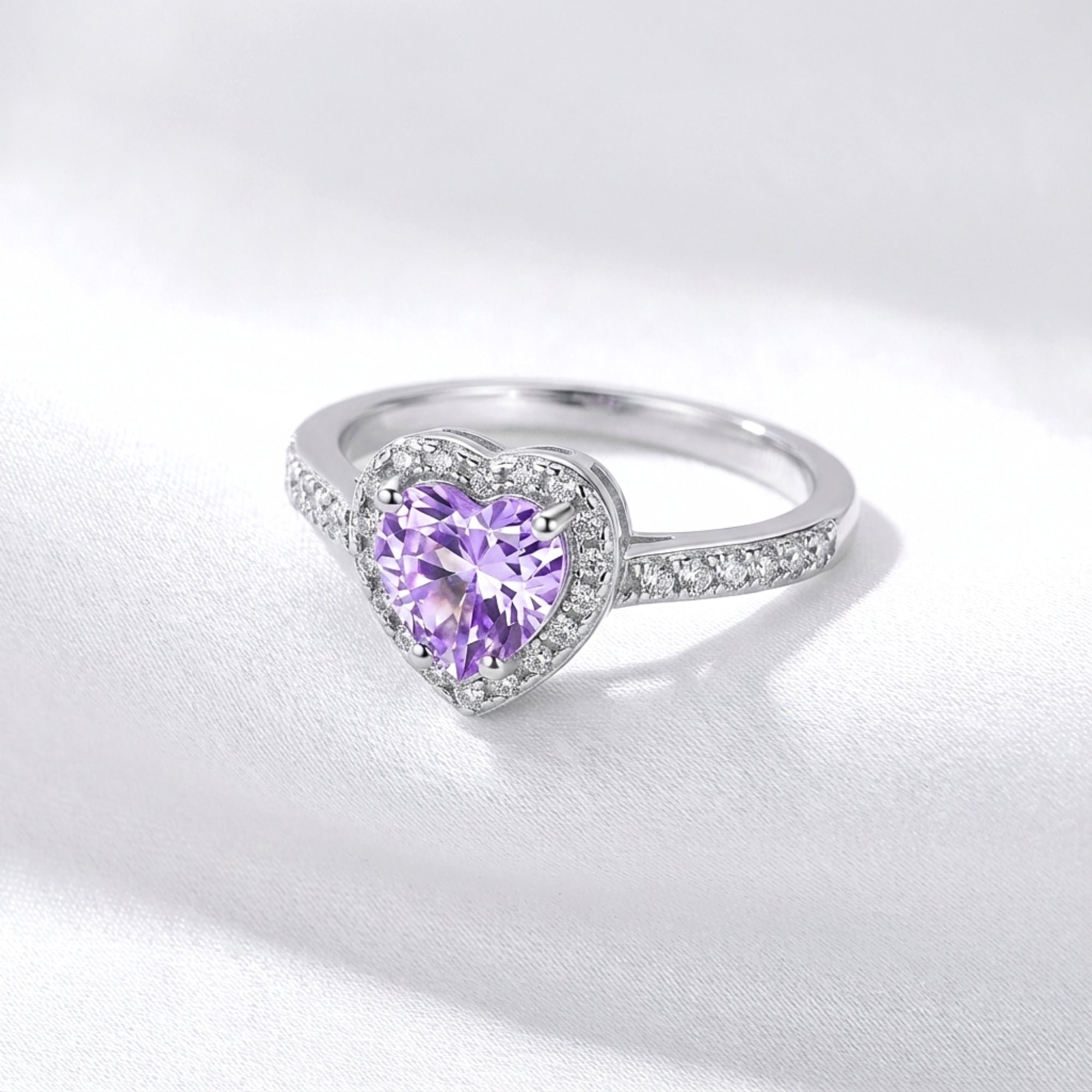 Side profile of the heart-cut purple amethyst S925 sterling silver ring resting on white silk-like fabric.