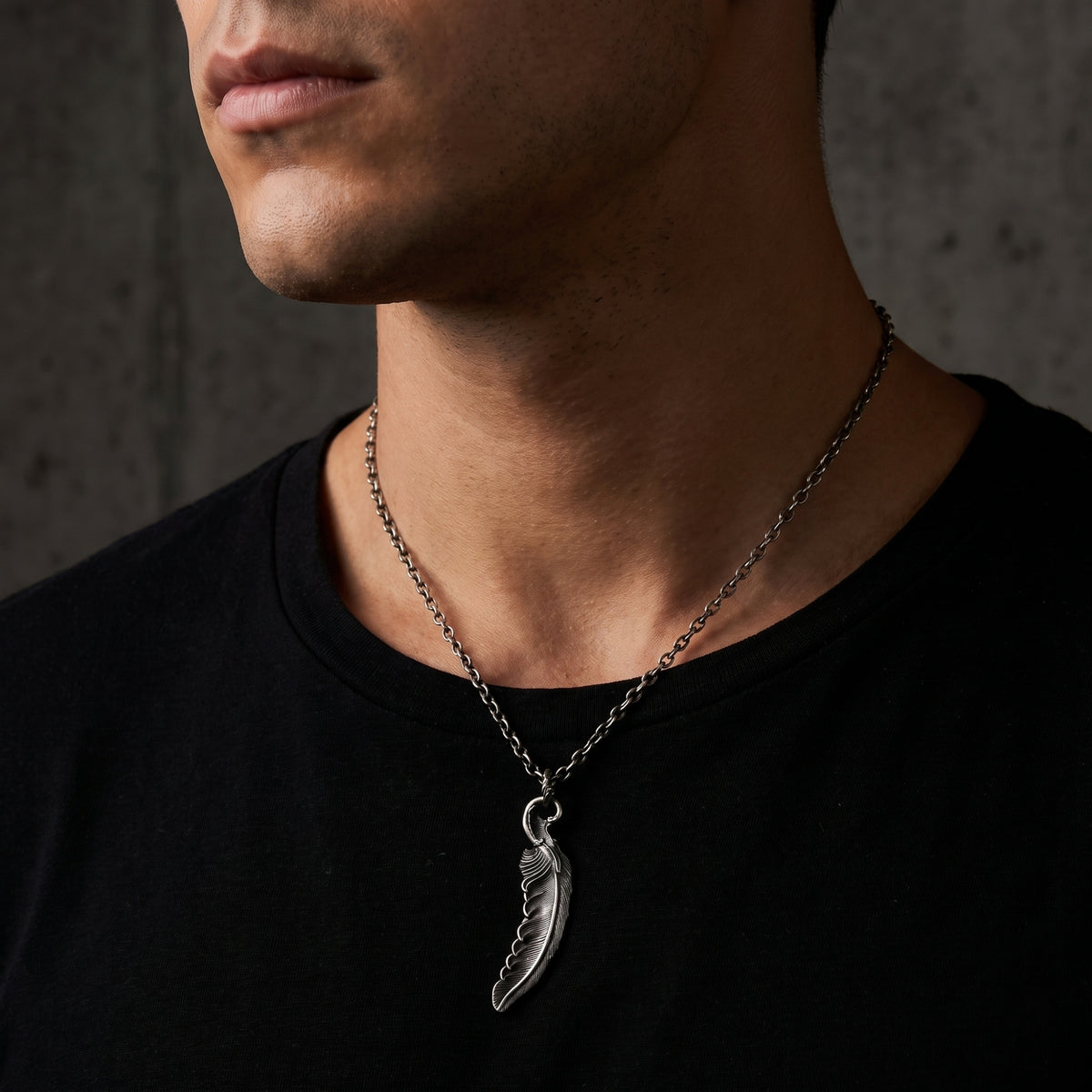 Model wearing the silver feather pendant necklace over a black crewneck shirt.