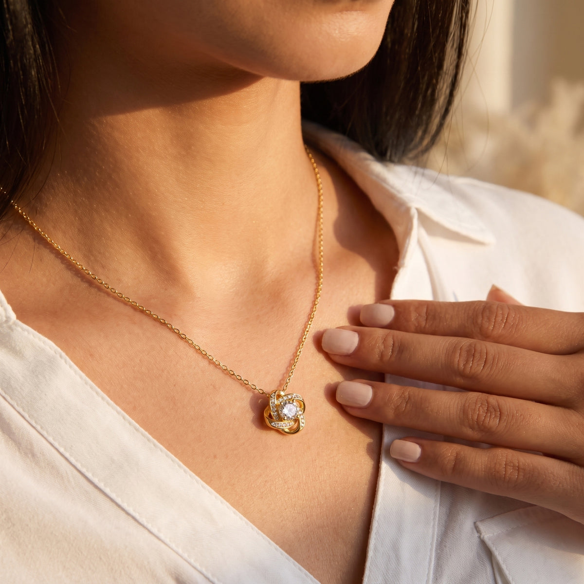Gold love knot necklace worn at the neckline.