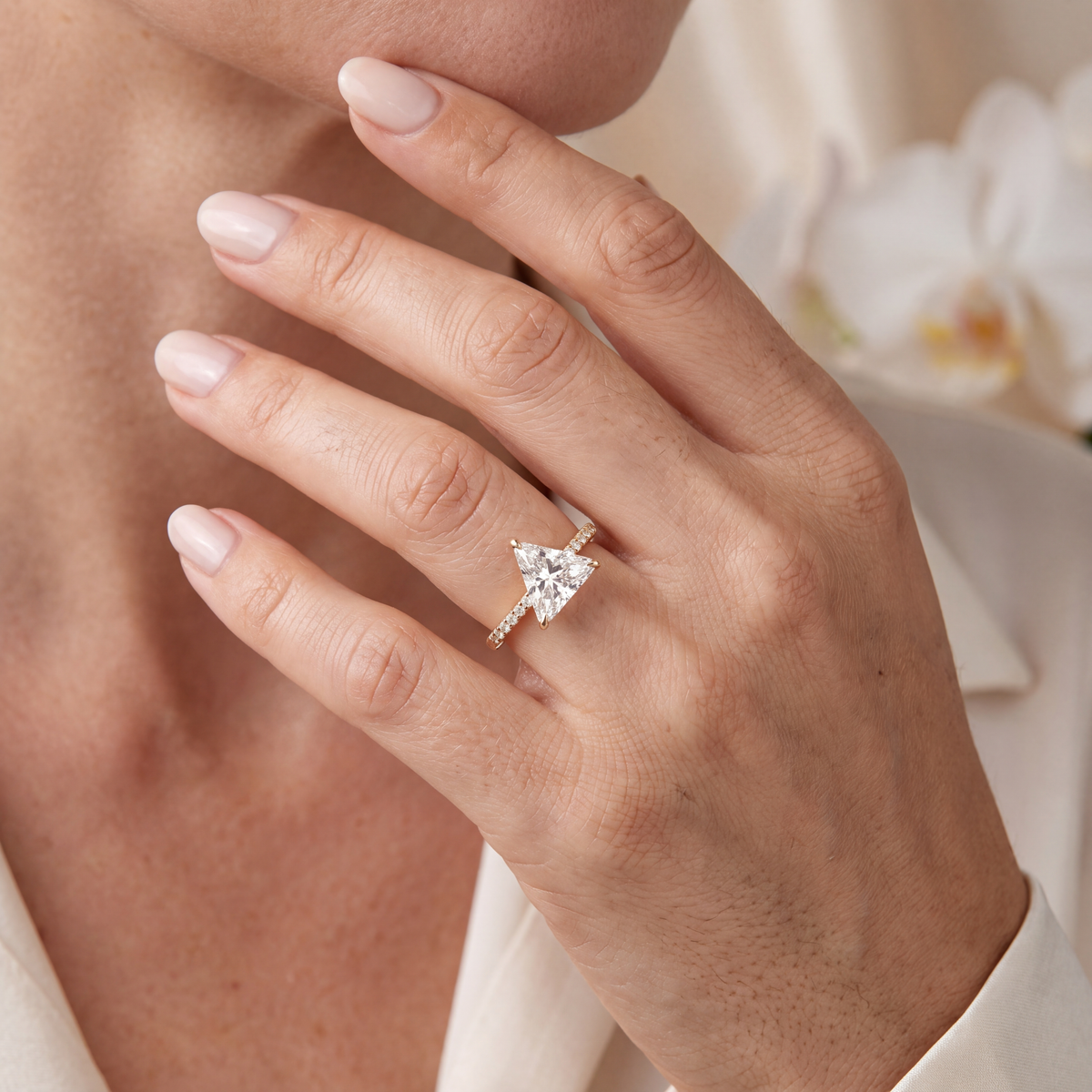 Gold trillion-cut moissanite engagement ring with a pavé band worn on a model's hand.