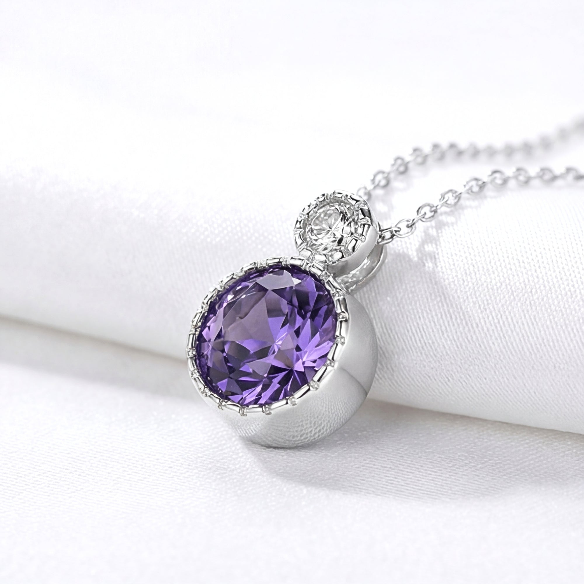 Side view detail of the round simulated amethyst pendant in sterling silver resting on soft white fabric.