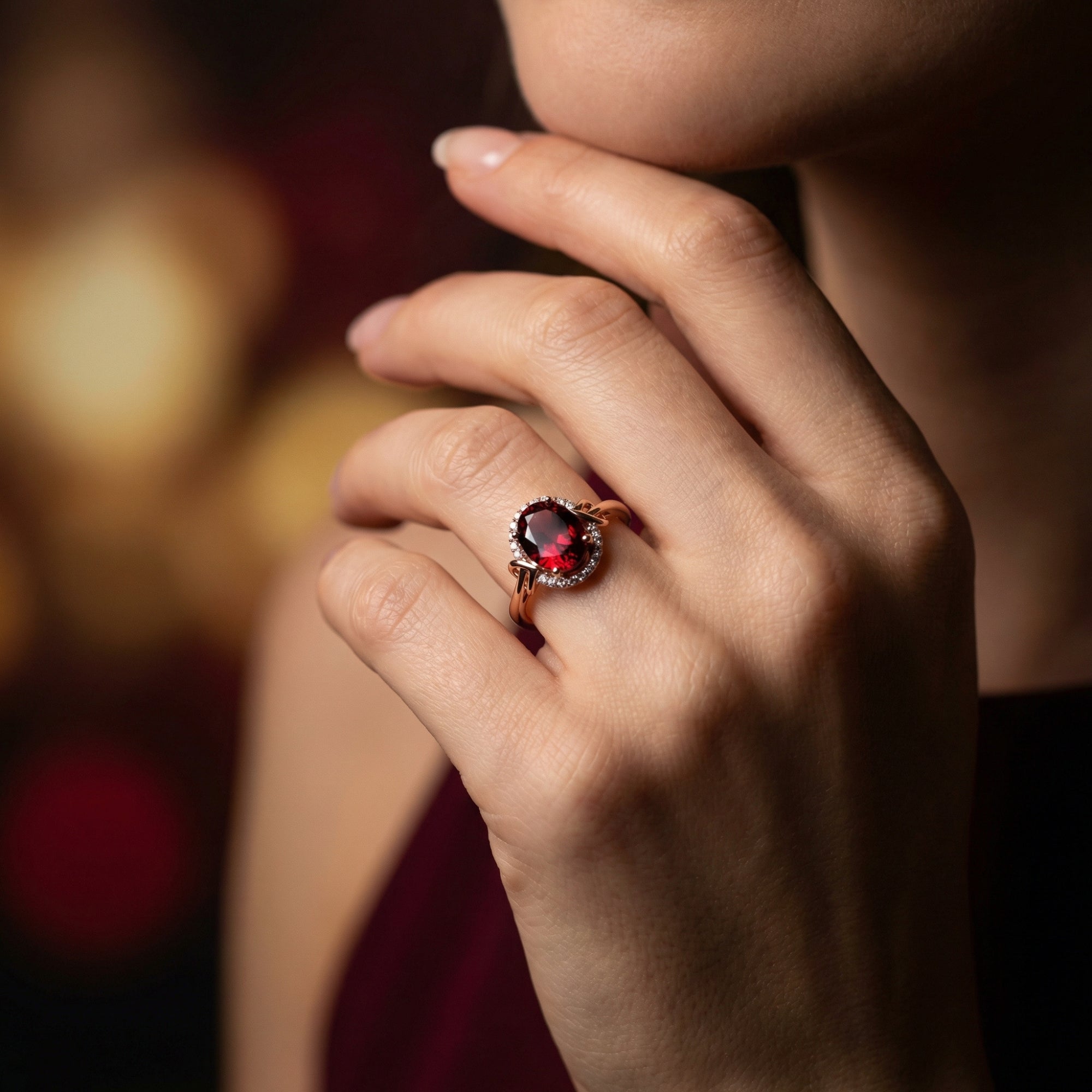 Woman wearing the oval garnet and rose gold halo ring on her finger, hand resting against her chin.