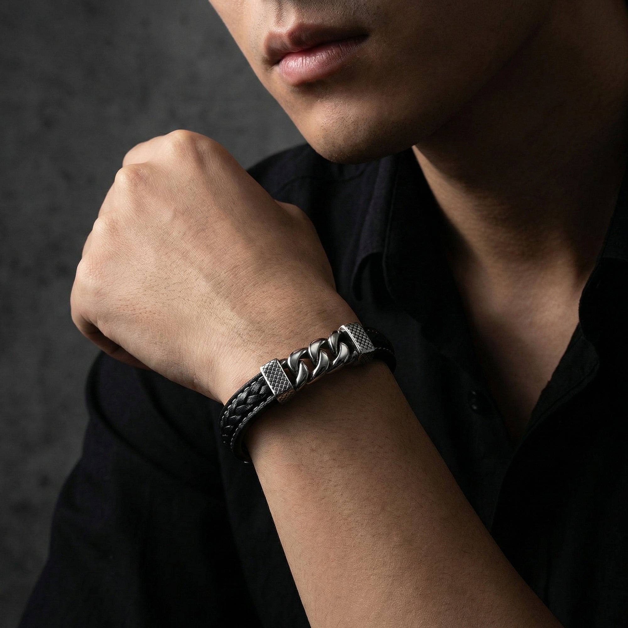 Men's braided black leather and silver steel link bracelet worn on a wrist by a model in a black shirt.