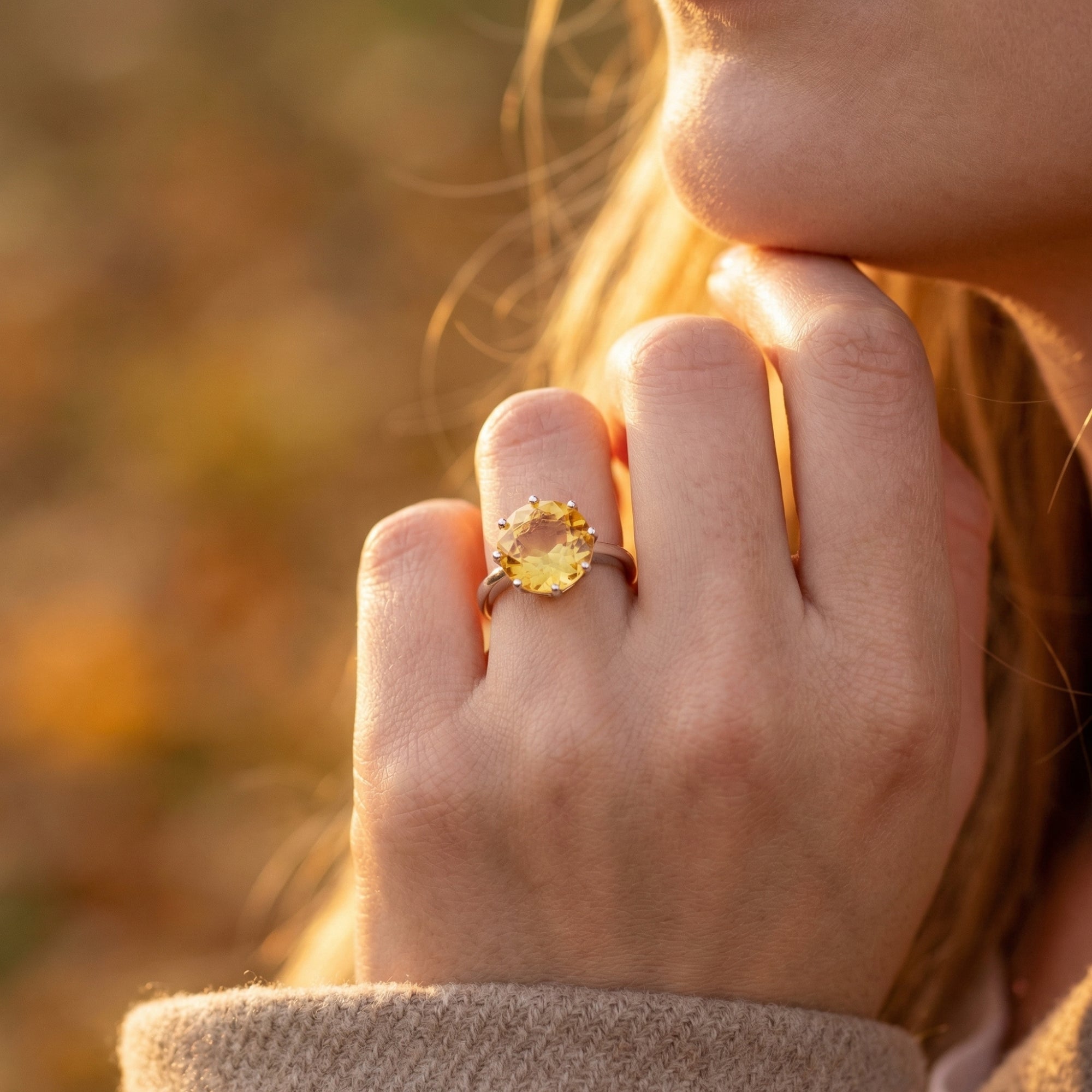 Large round-cut citrine ring in sterling silver worn on a woman's hand in warm outdoor light.