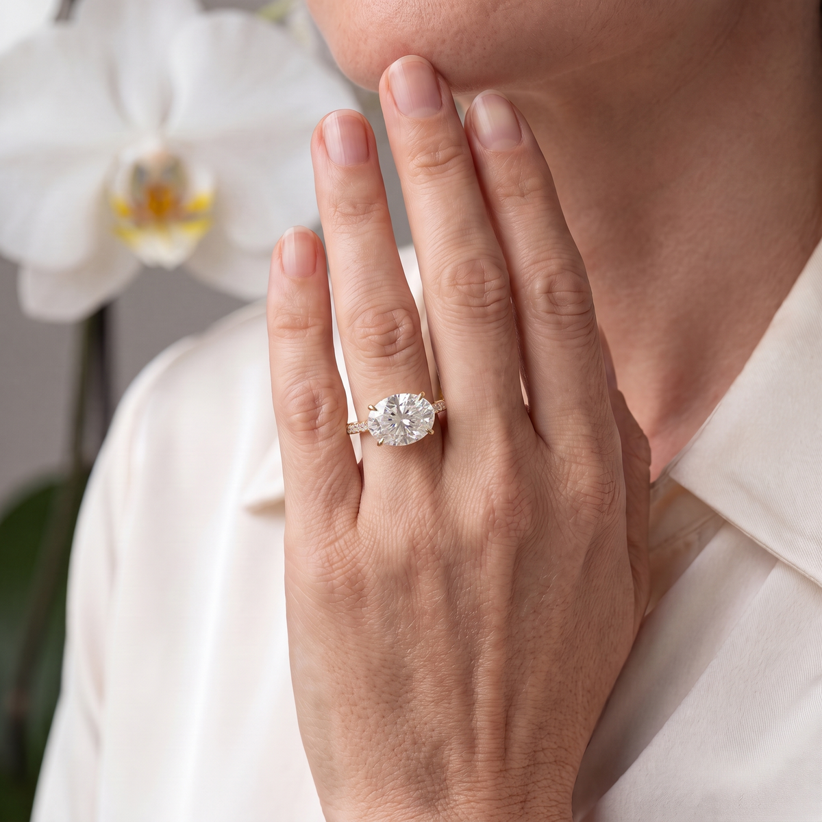 A lifestyle view of an East-West oval cut moissanite engagement ring in yellow gold worn on a model's hand.