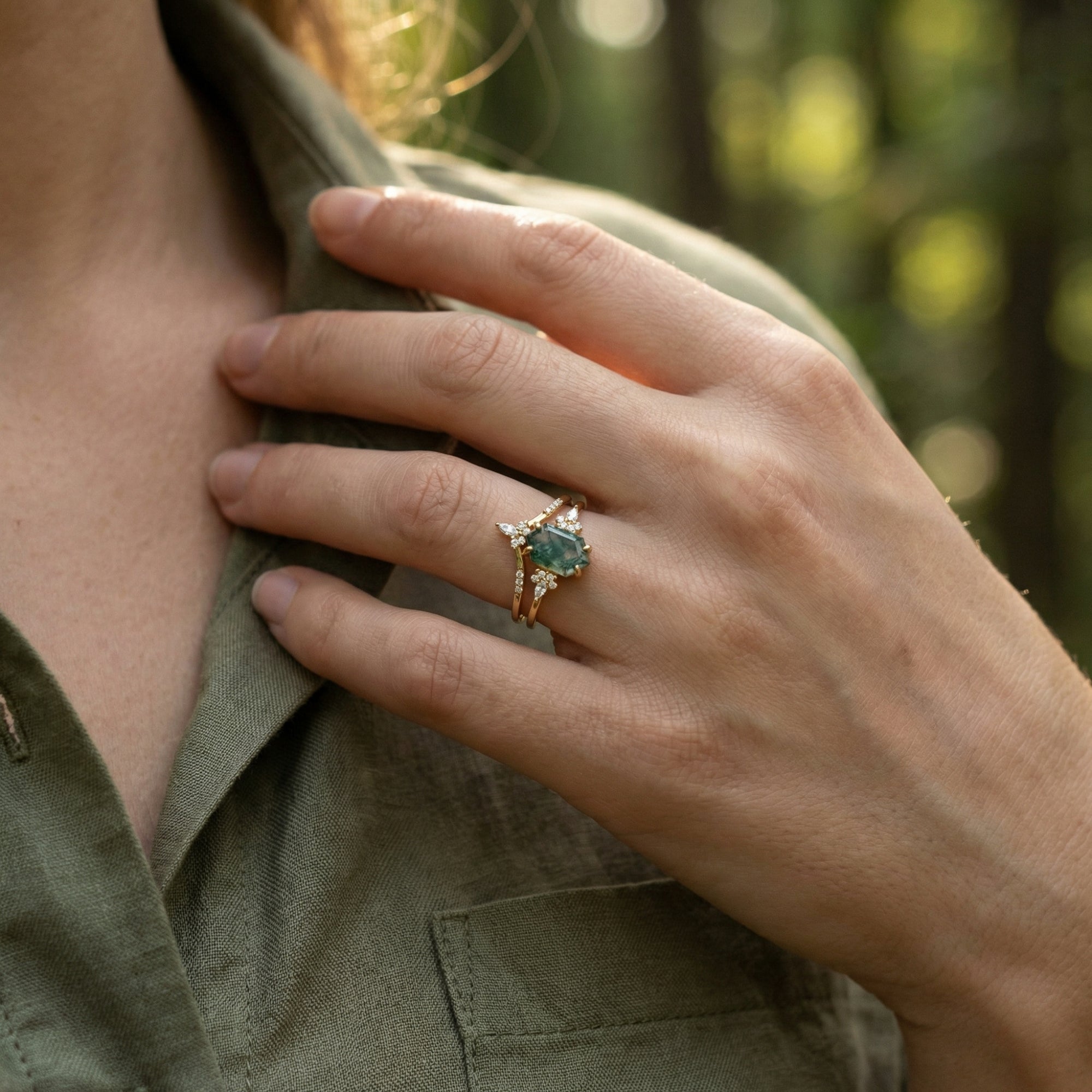 Gold-plated moss agate ring set worn on a hand against a green linen shirt in natural light.