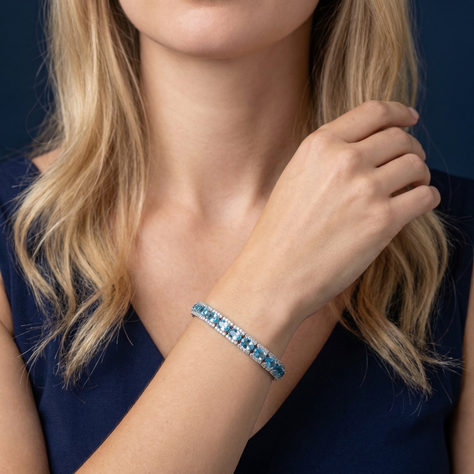 Woman wearing the Oceanica natural blue topaz tennis bracelet in white gold on her wrist.