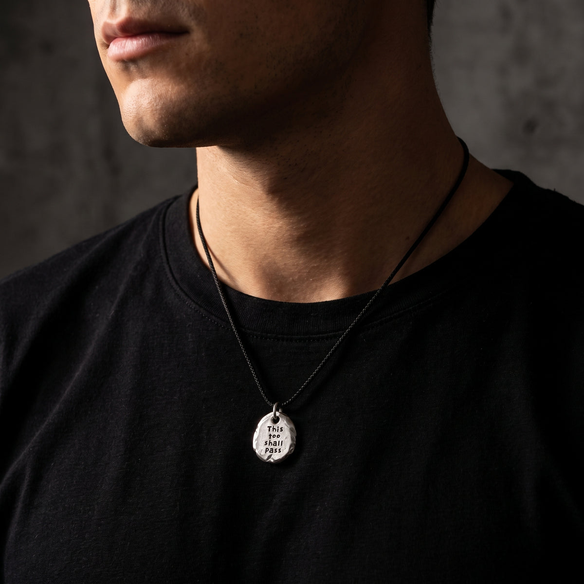 Man wearing the engraved silver pebble pendant on a black cord over a black shirt.