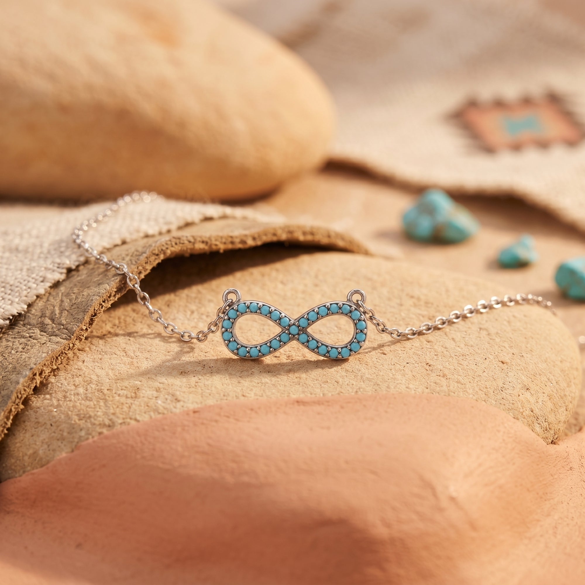 Close-up of a silver infinity pendant set with round turquoise stones, resting on a smooth desert rock.