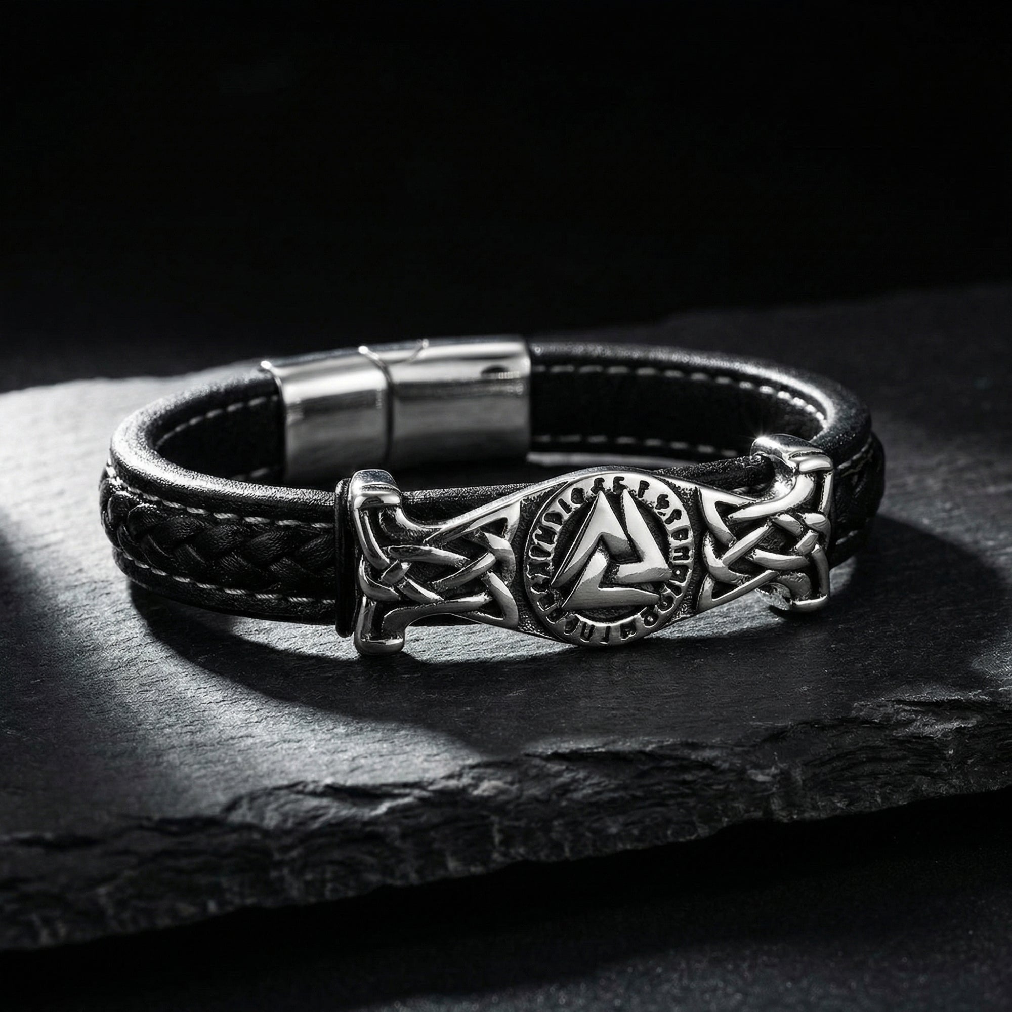 Close-up of the stainless steel Valknut and rune casting on a black braided leather men's bracelet.