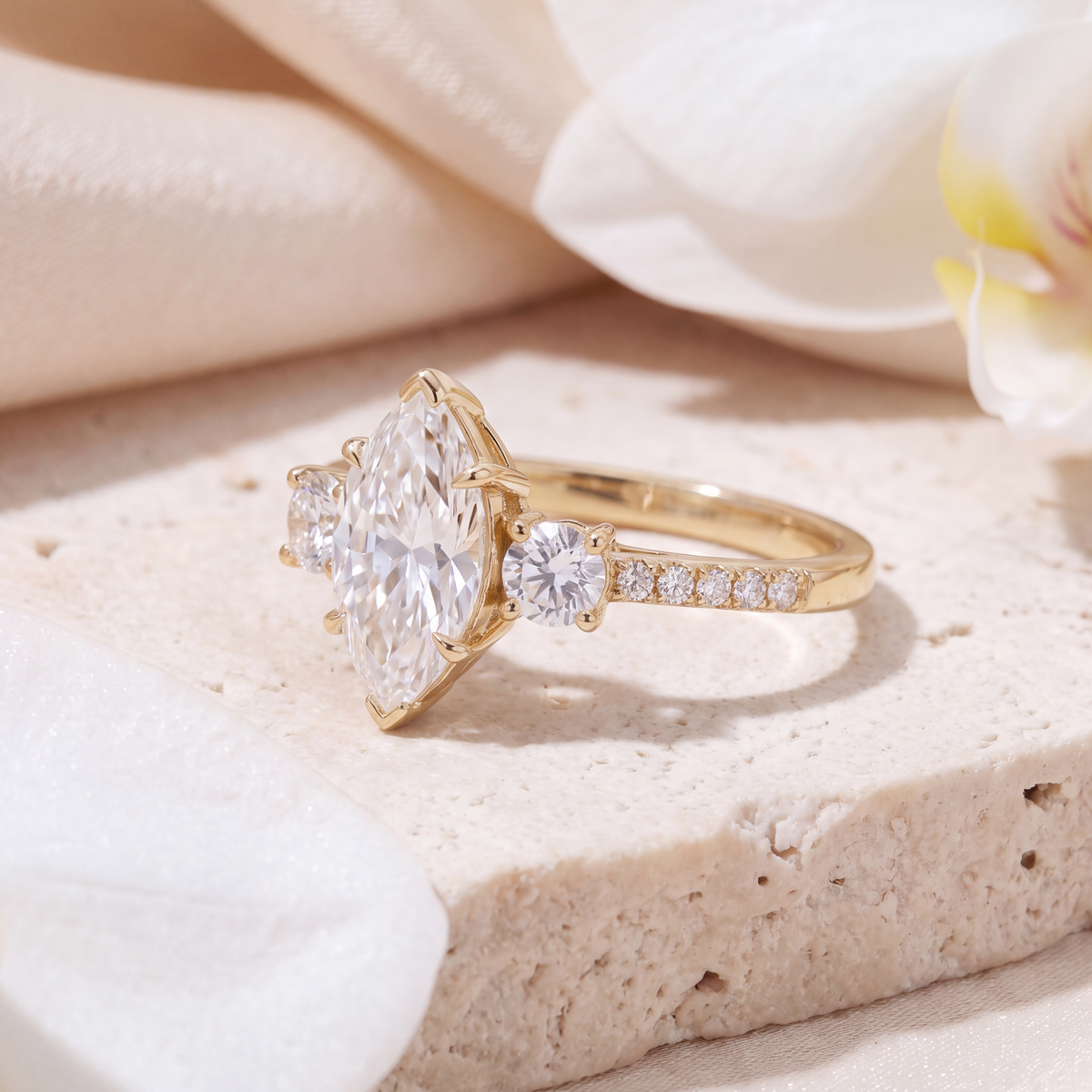 Angled profile view of the marquise moissanite three-stone ring with side accent stones in yellow gold.