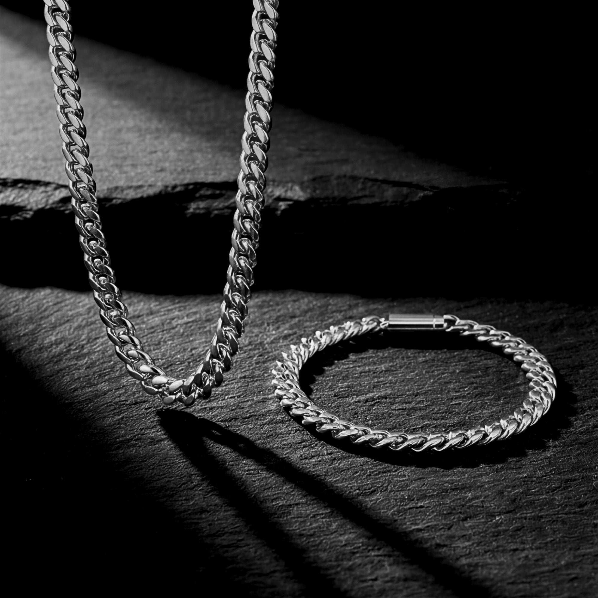 Silver 6mm Cuban link chain and bracelet set draped on a dark slate surface.