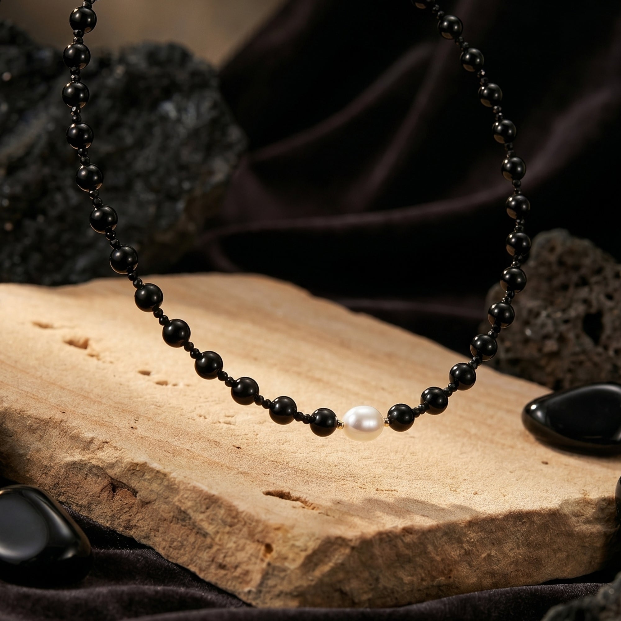 Detailed view of a white pearl and round black onyx beads on an 18K gold plated necklace.