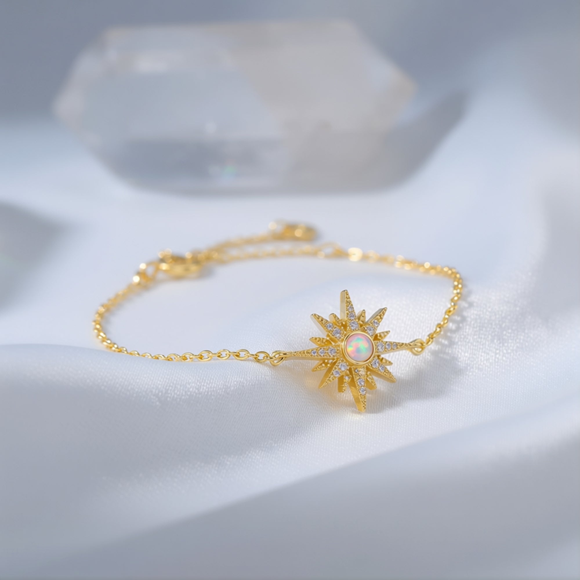 Angled view of the Elowen gold-tone sterling silver starburst bracelet with a round-cut white opal on fabric.