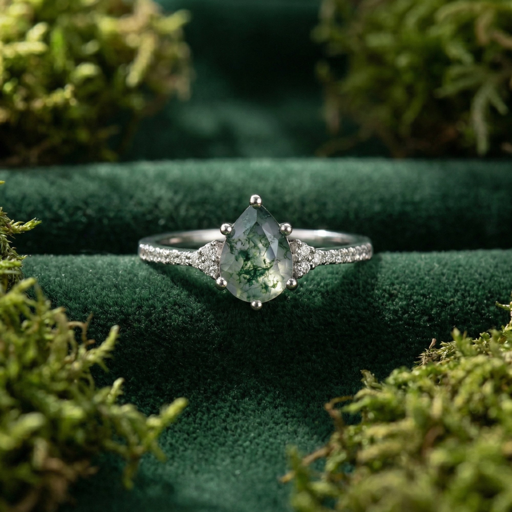 Front view macro shot of a pear cut moss agate solitaire ring with diamond accents on green velvet.