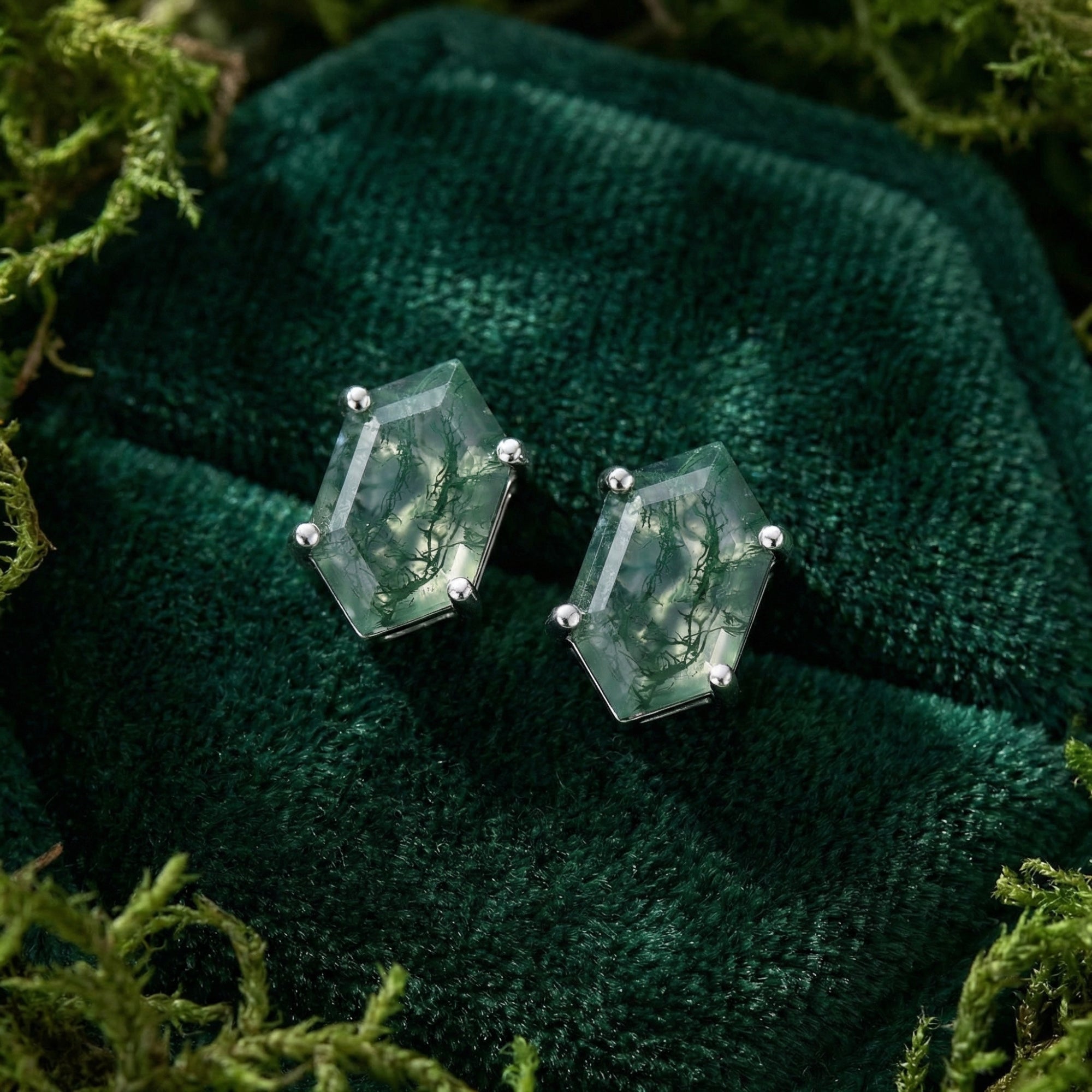 Close-up of hexagon-cut moss agate stud earrings in sterling silver settings on dark green velvet.