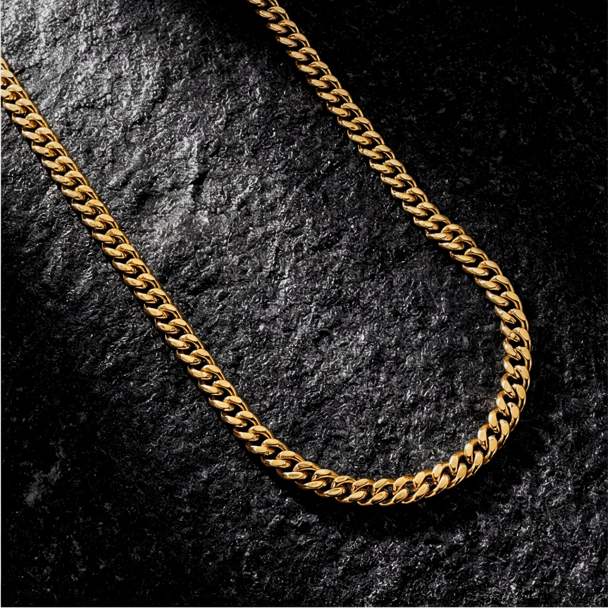 Top-down view of a 4mm gold stainless steel Cuban chain necklace on a dark, textured stone surface.
