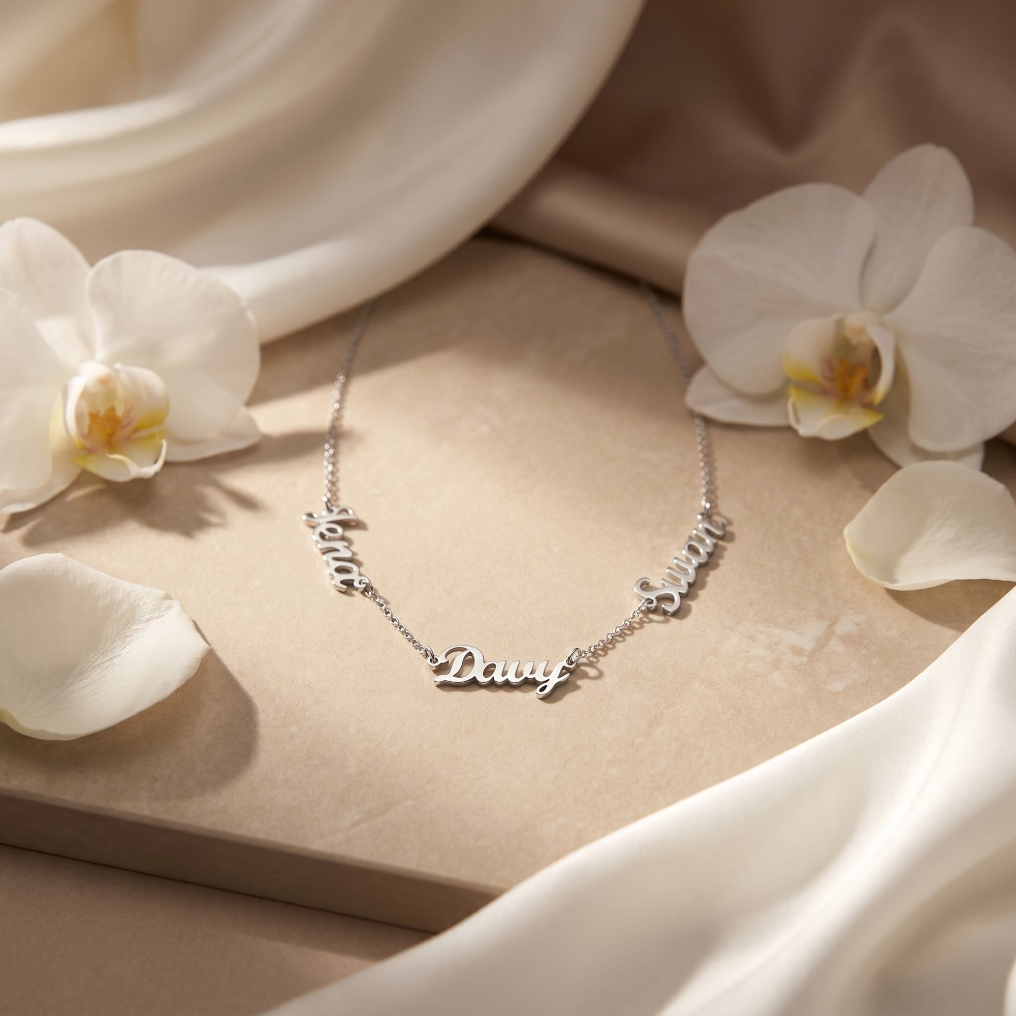 Silver PVD stainless steel name necklace on stone surface with white orchids.