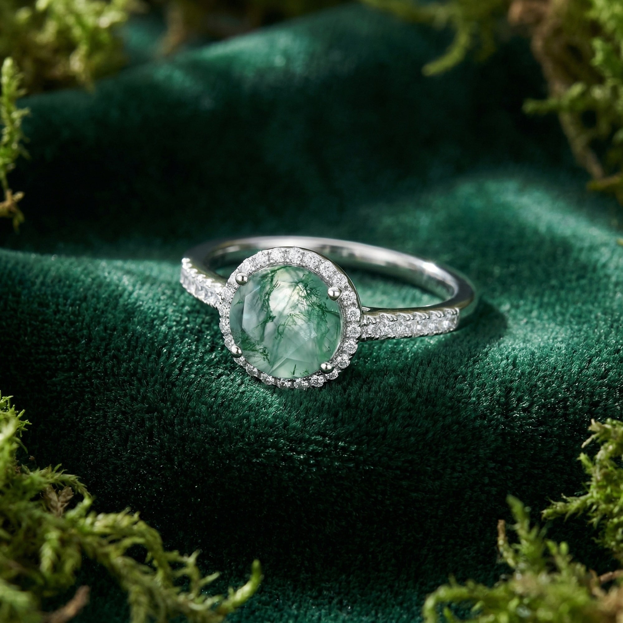 Sterling silver moss agate ring with diamond accents resting on green velvet surrounded by natural moss.