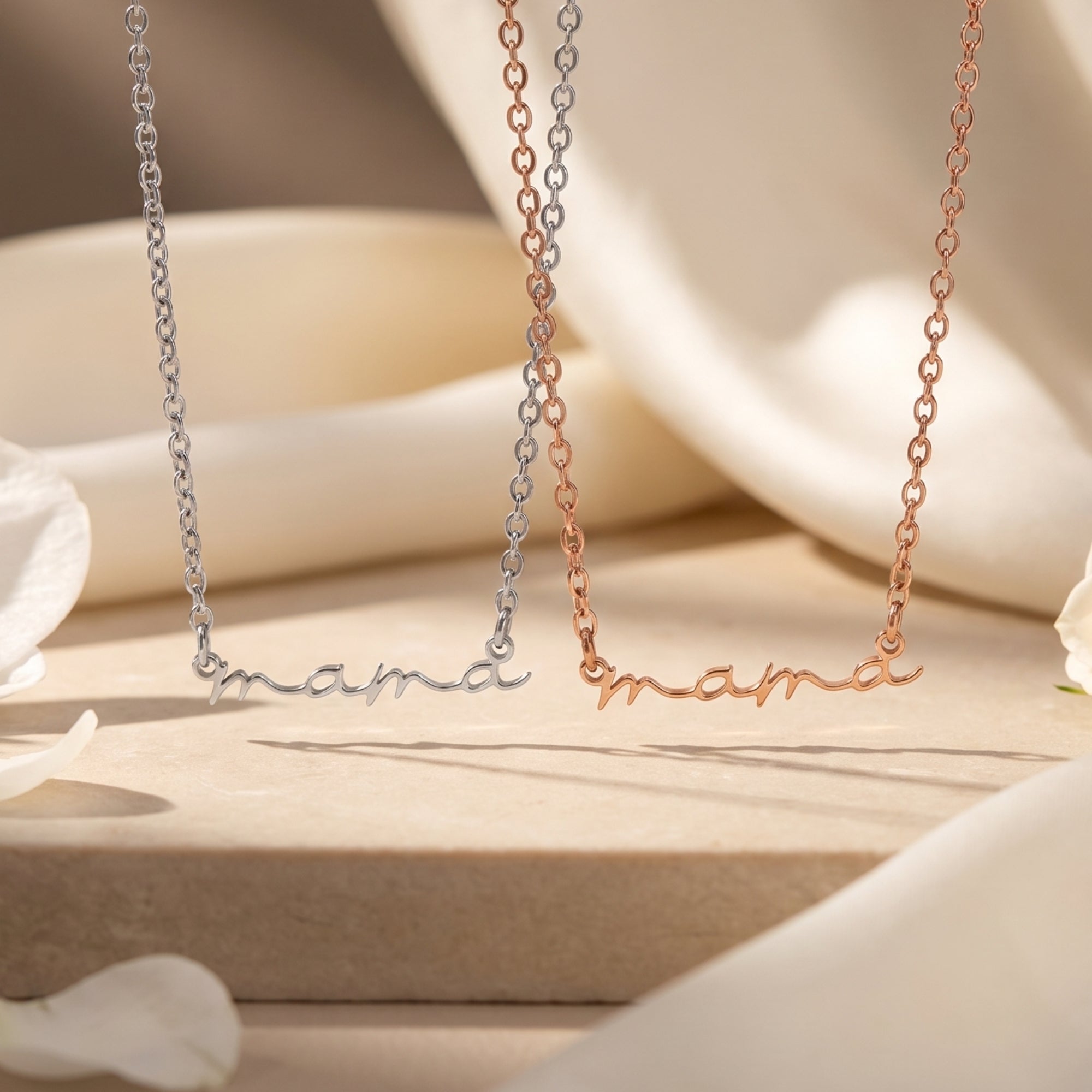 Silver and rose gold mama script necklaces on a neutral surface.