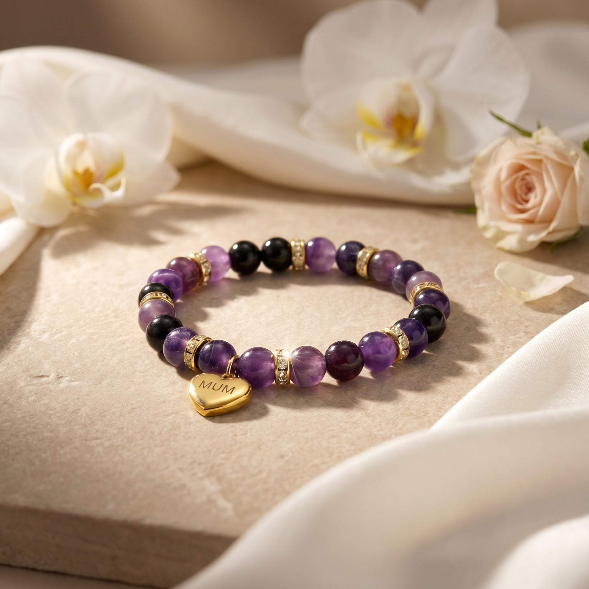Amethyst beaded bracelet with 18K gold finish heart charm on a stone surface.