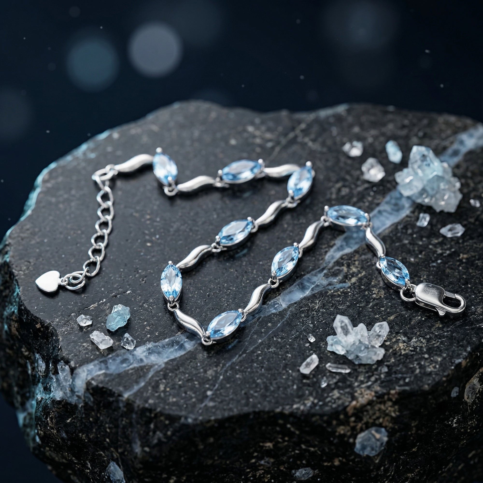 Silver marquise natural blue topaz bracelet laid out on a dark rock, showing the lobster clasp and heart charm.