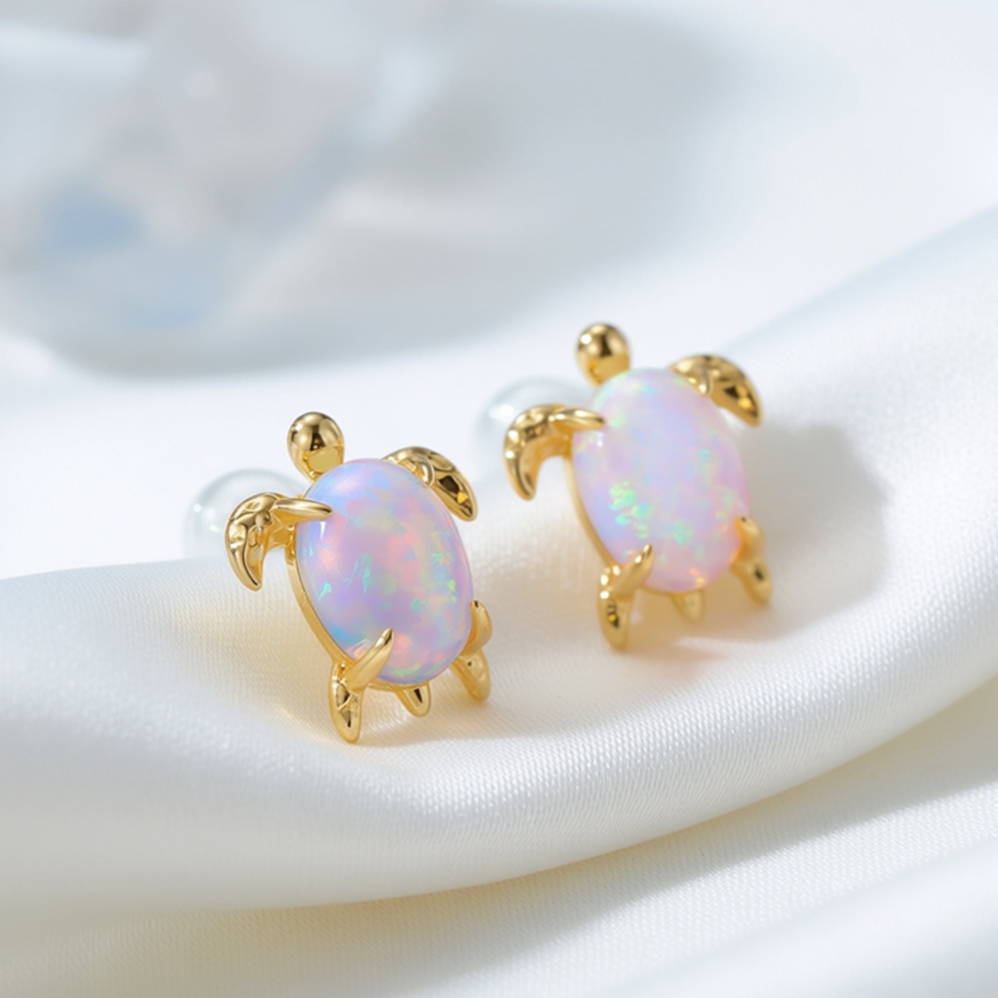 Close-up of gold-tone turtle stud earrings featuring oval white opals with iridescent play-of-color.