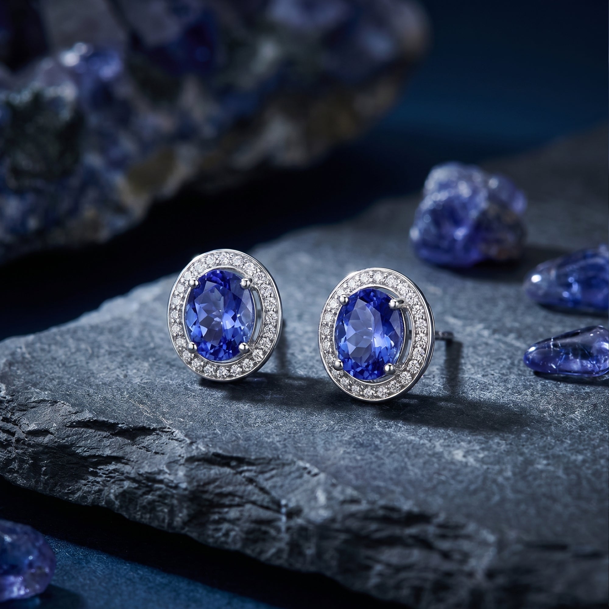 Close-up of oval natural tanzanite stud earrings in 18K white gold with diamond halos on a textured rock surface.