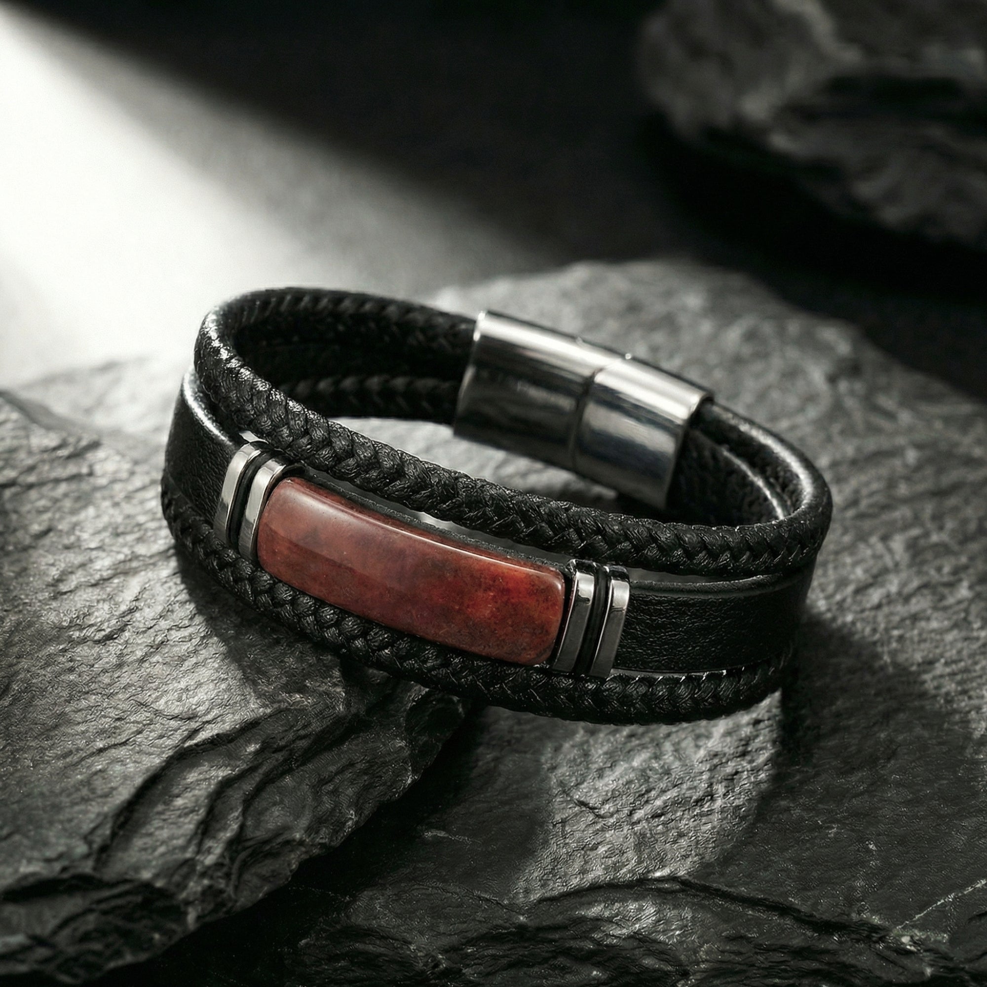 Close-up of the Apex bracelet's black magnetic clasp and red stone centerpiece on a dark stone background.