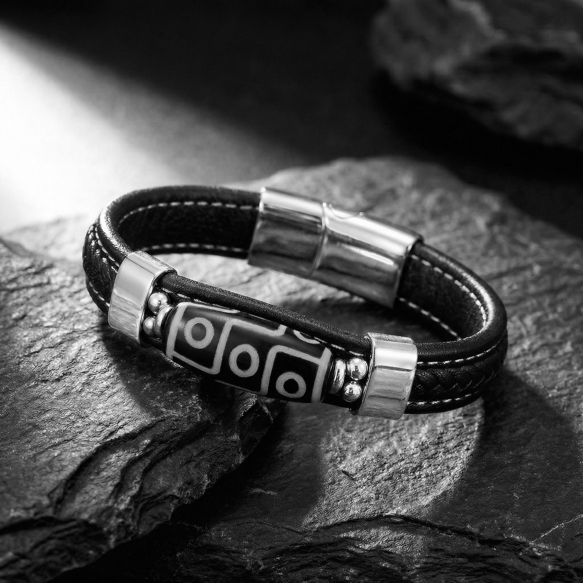 Side view of the Echelon black leather bracelet with silver-tone steel centerpiece on textured stone.