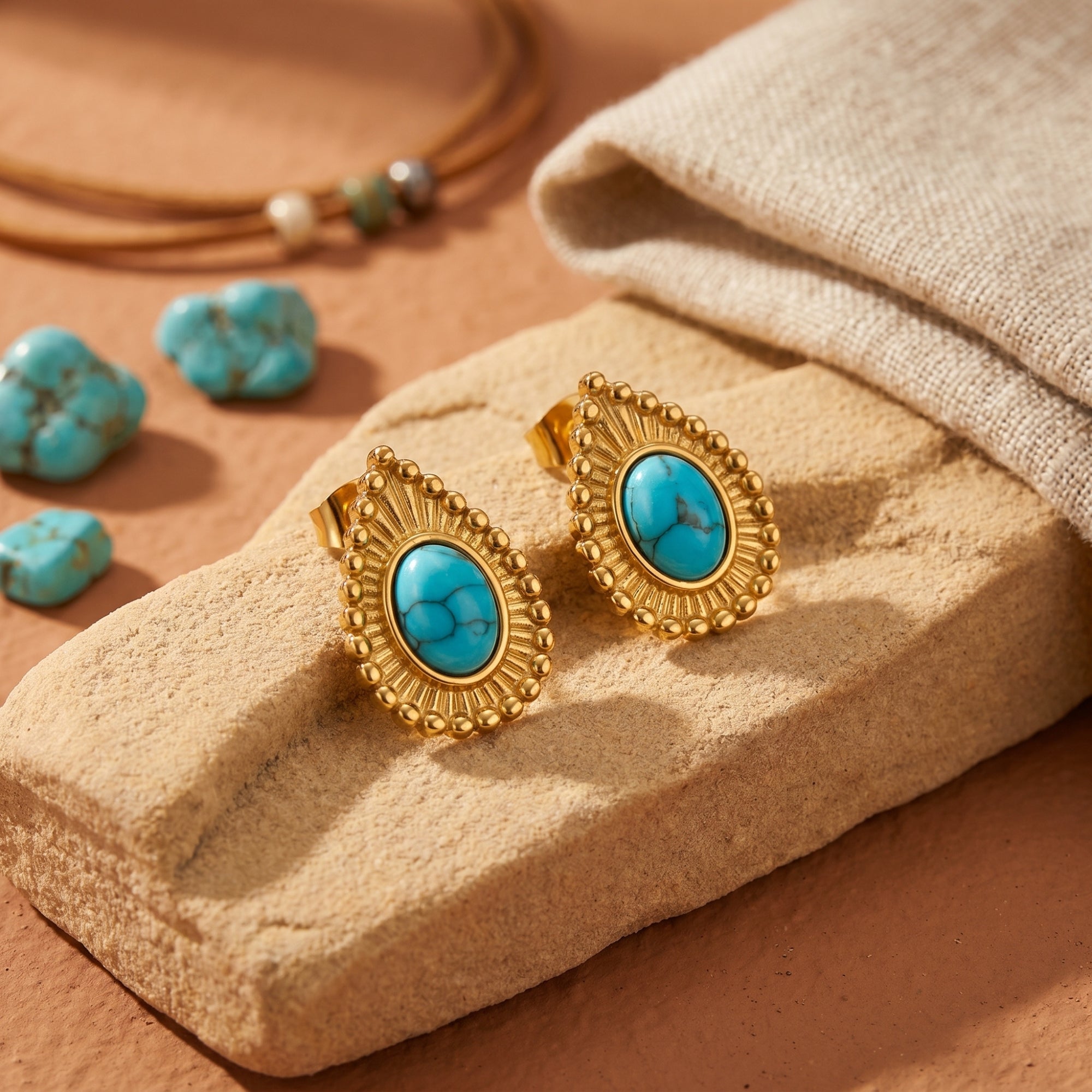 Close-up of turquoise oval cabochon earrings featuring a detailed 18K gold beaded border on a textured stone.