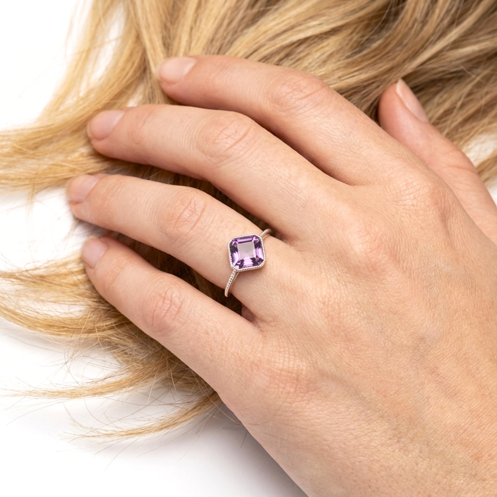 Cushion-cut simulated amethyst sterling silver ring worn on a woman's hand against blonde hair.