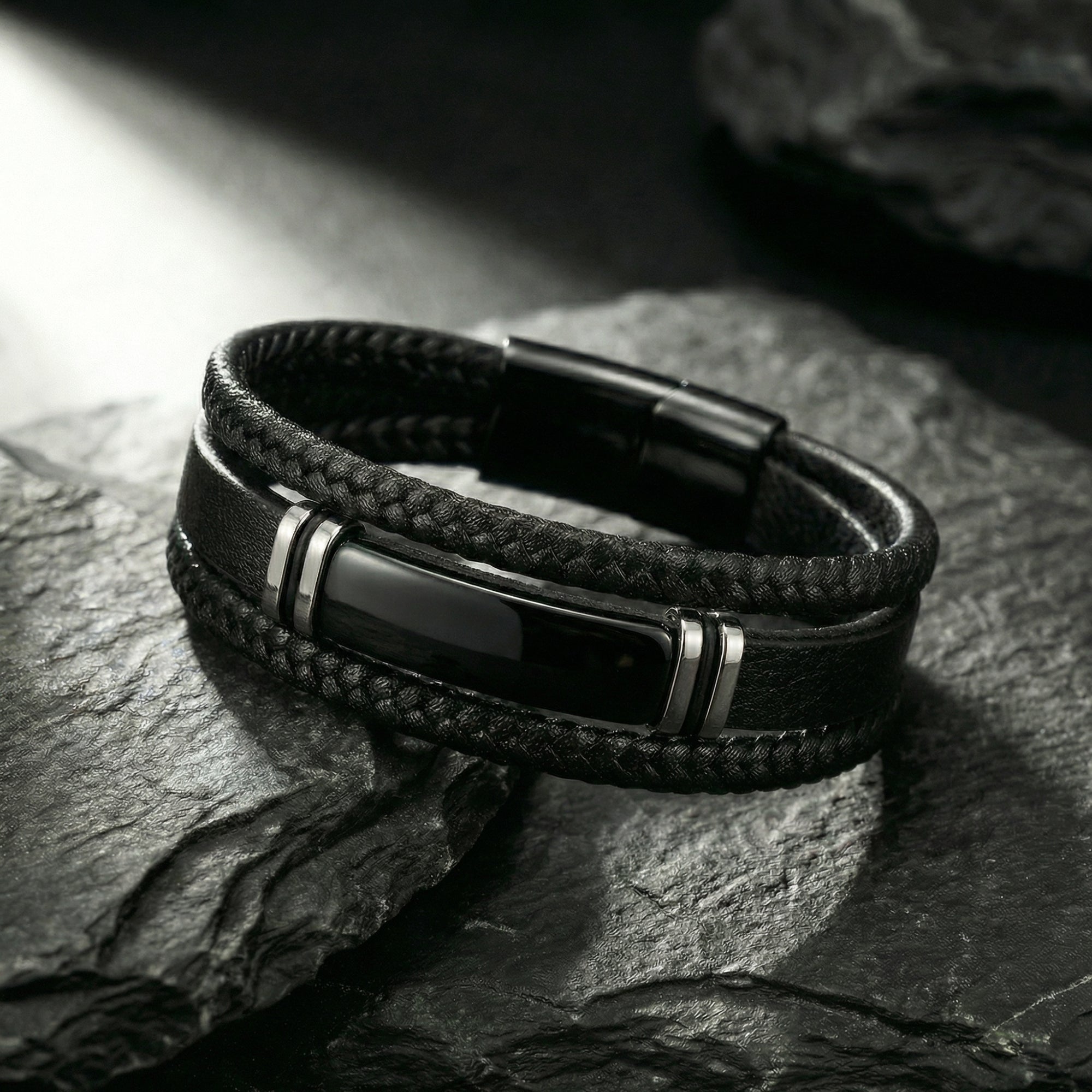 Close-up of the black stainless steel center bar and braided leather strands of the Phantom Bracelet on a rock.