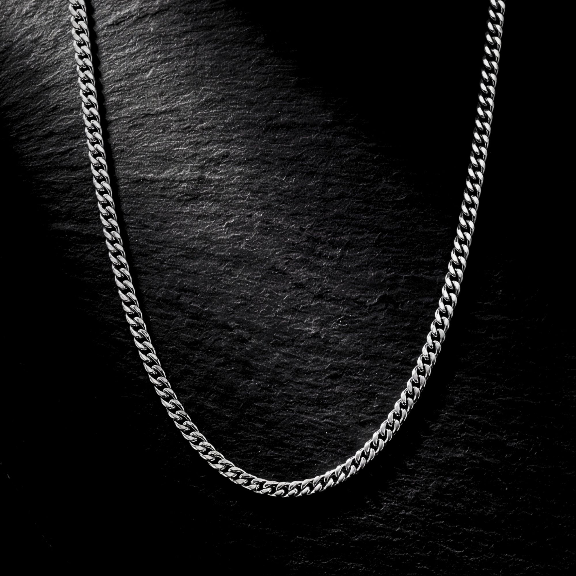 Close-up detail of the 2mm silver stainless steel curb chain links on a dark stone surface.