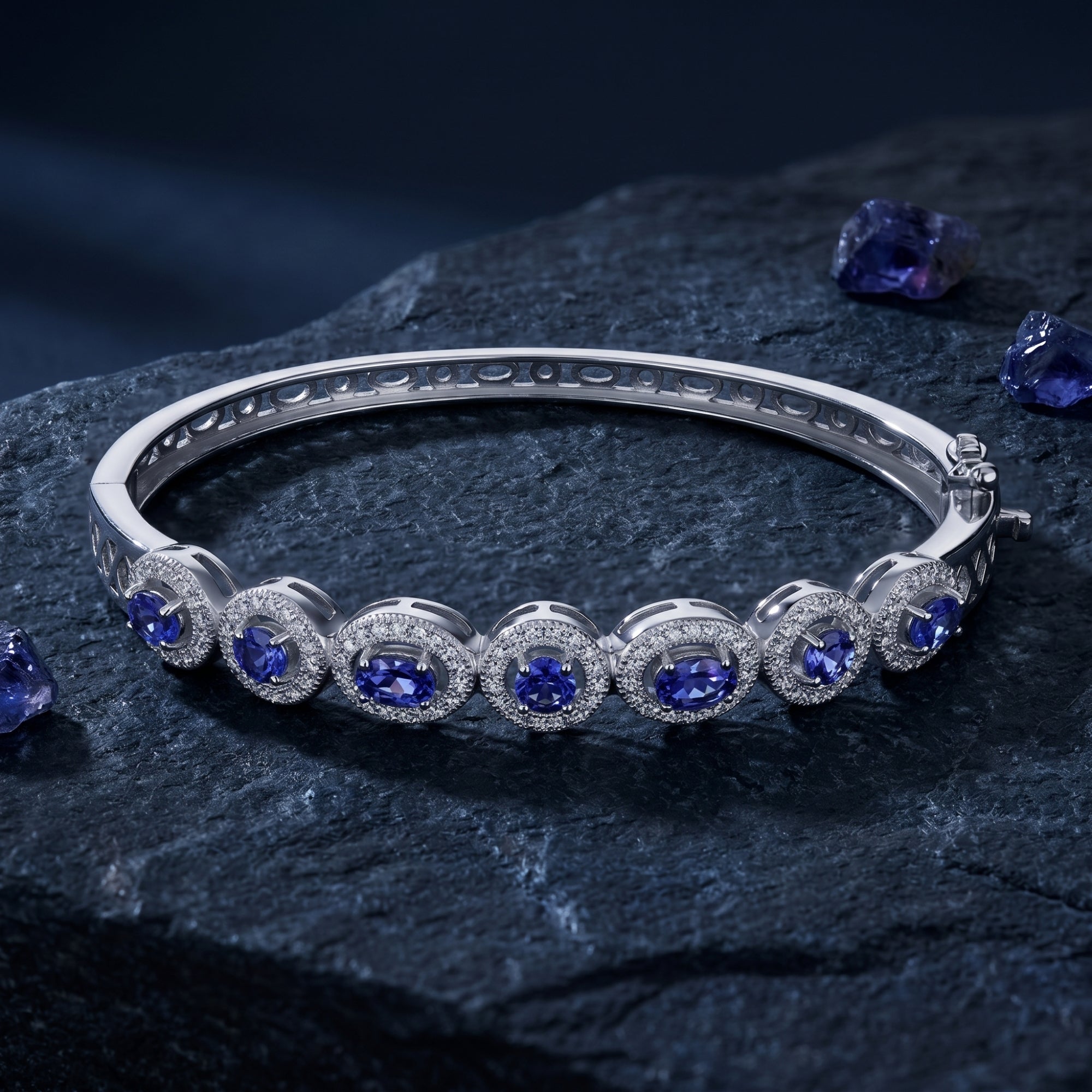 Sterling silver tanzanite line bracelet with oval and round stones displayed on a textured dark rock surface.