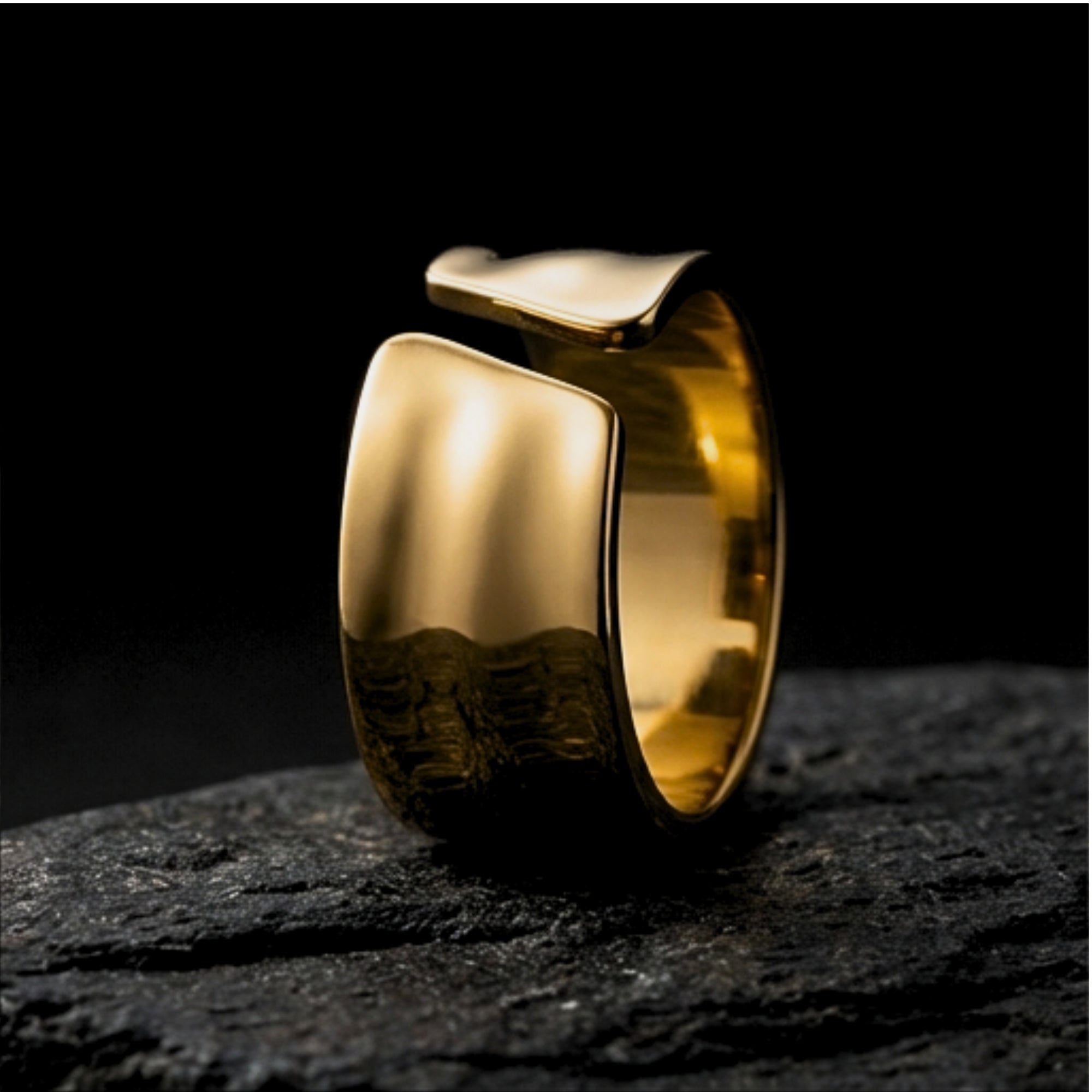 Side view of the gold stainless steel Origin Flow band ring on a dark stone background, showing its polished finish.