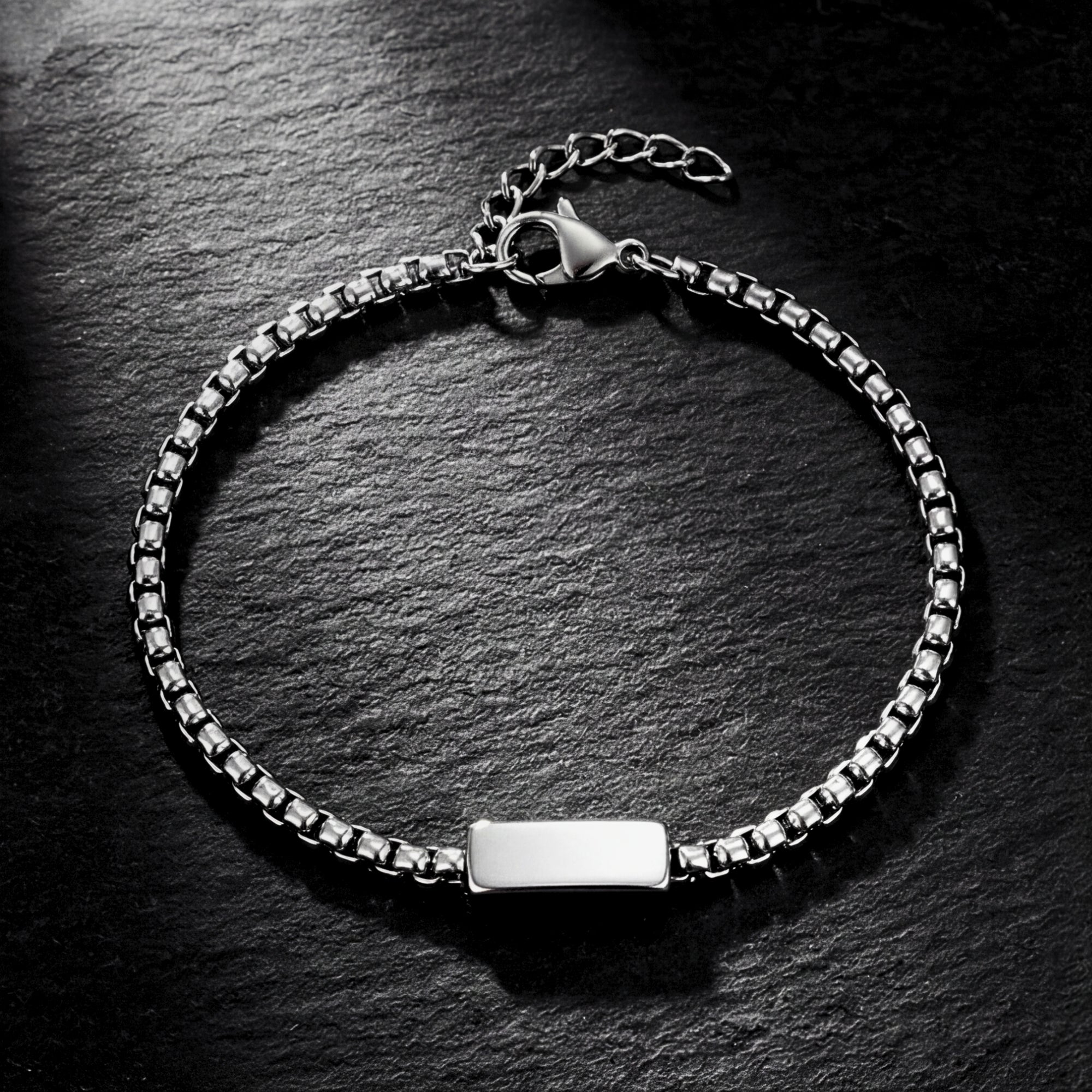 Overhead flat lay of a 5mm polished silver stainless steel link ID bracelet on a dark slate background.