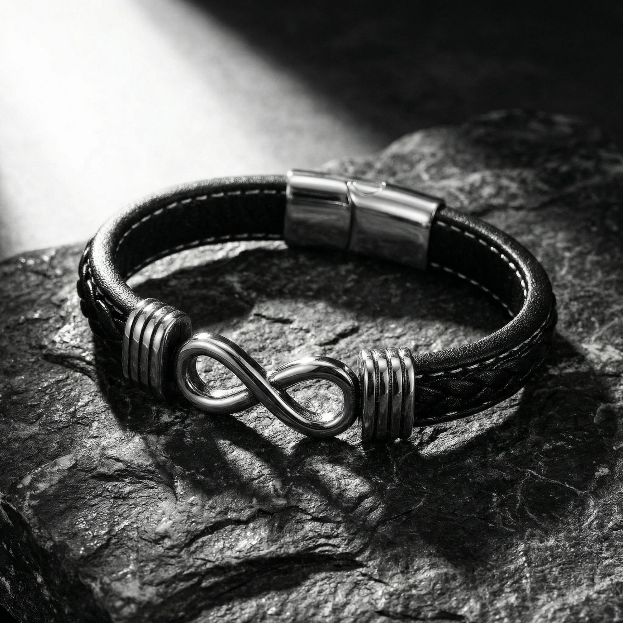 Close-up of a men's black braided leather bracelet with a silver stainless steel infinity clasp on stone.