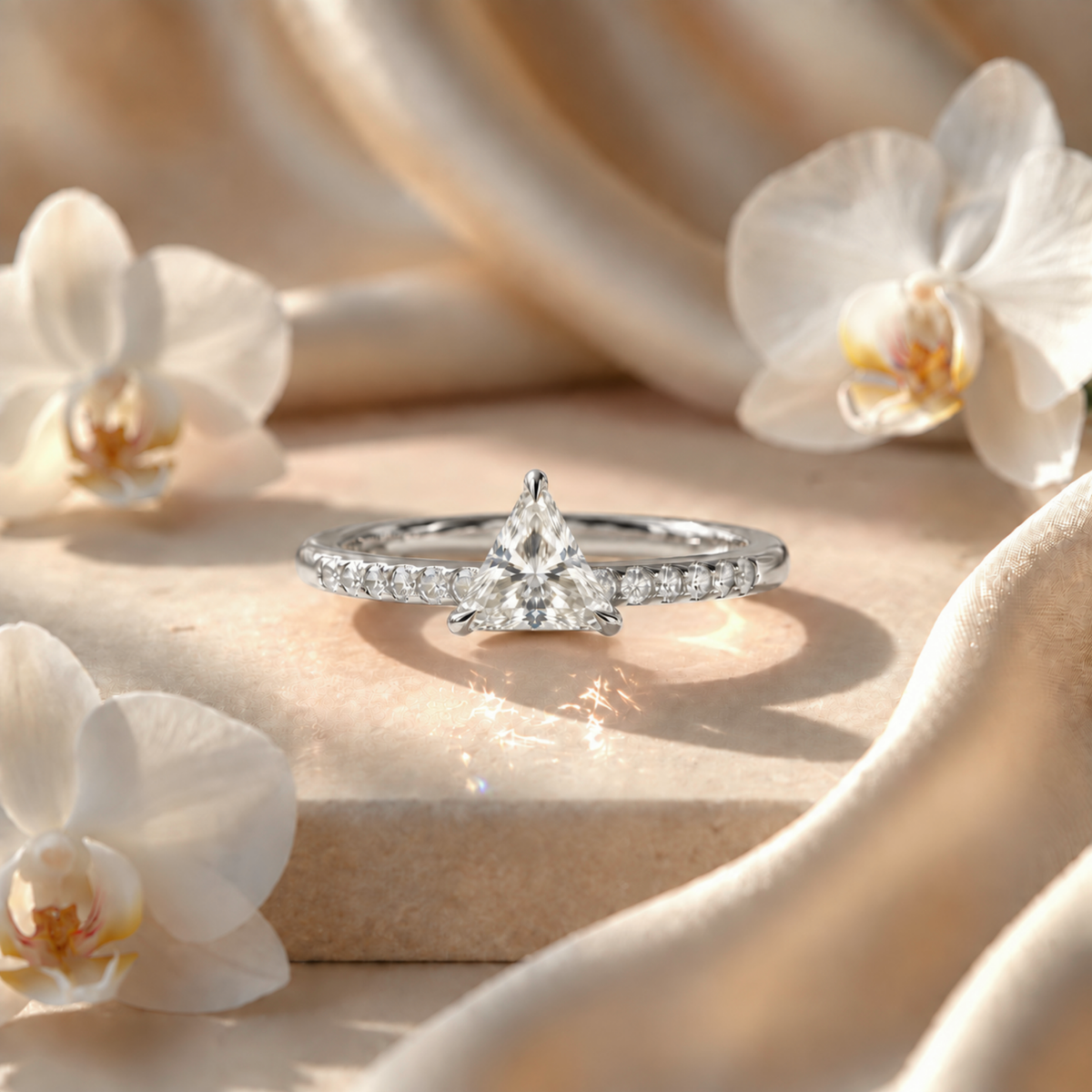 White gold trillion-cut moissanite engagement ring on a decorative stone pedestal.