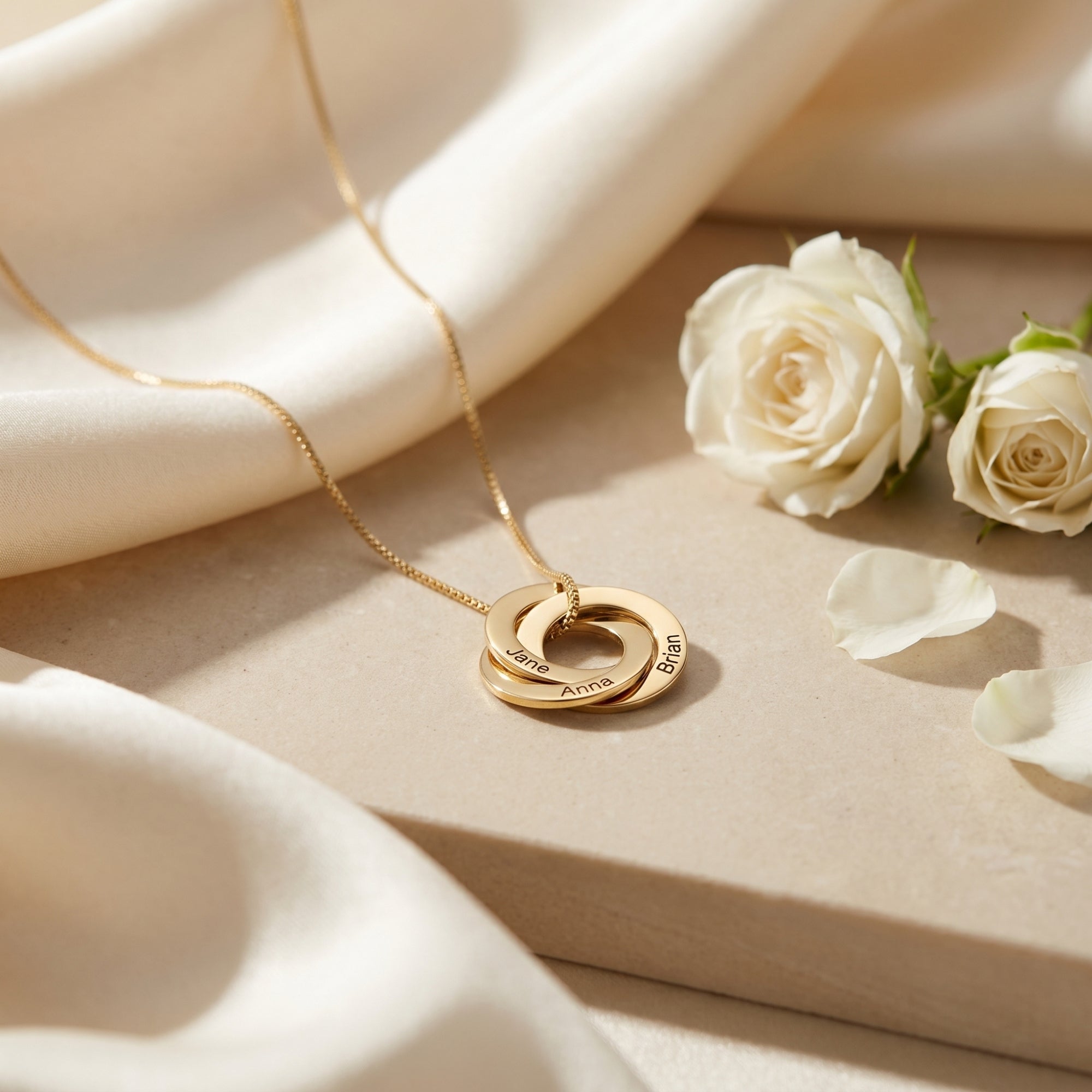 Gold Camilla necklace with three interlocked name rings on stone with white roses.