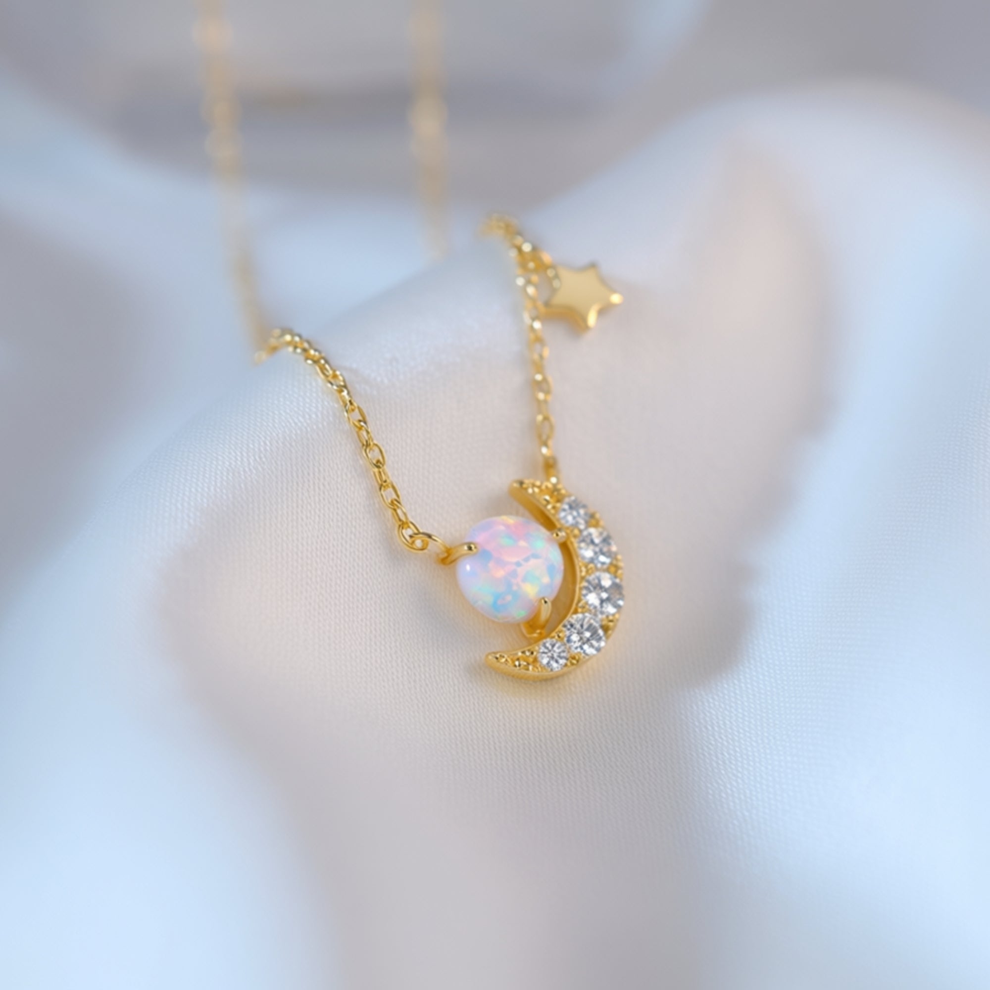 Close-up of a round white opal and crystal-accented crescent moon pendant on a gold vermeil chain.