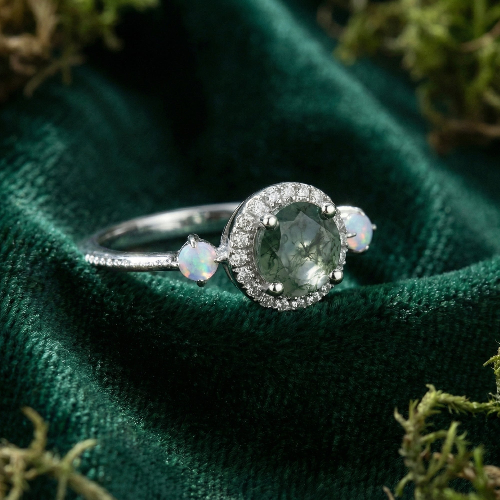 Macro shot of a round cut natural moss agate ring with a diamond halo and opal accents on green velvet.