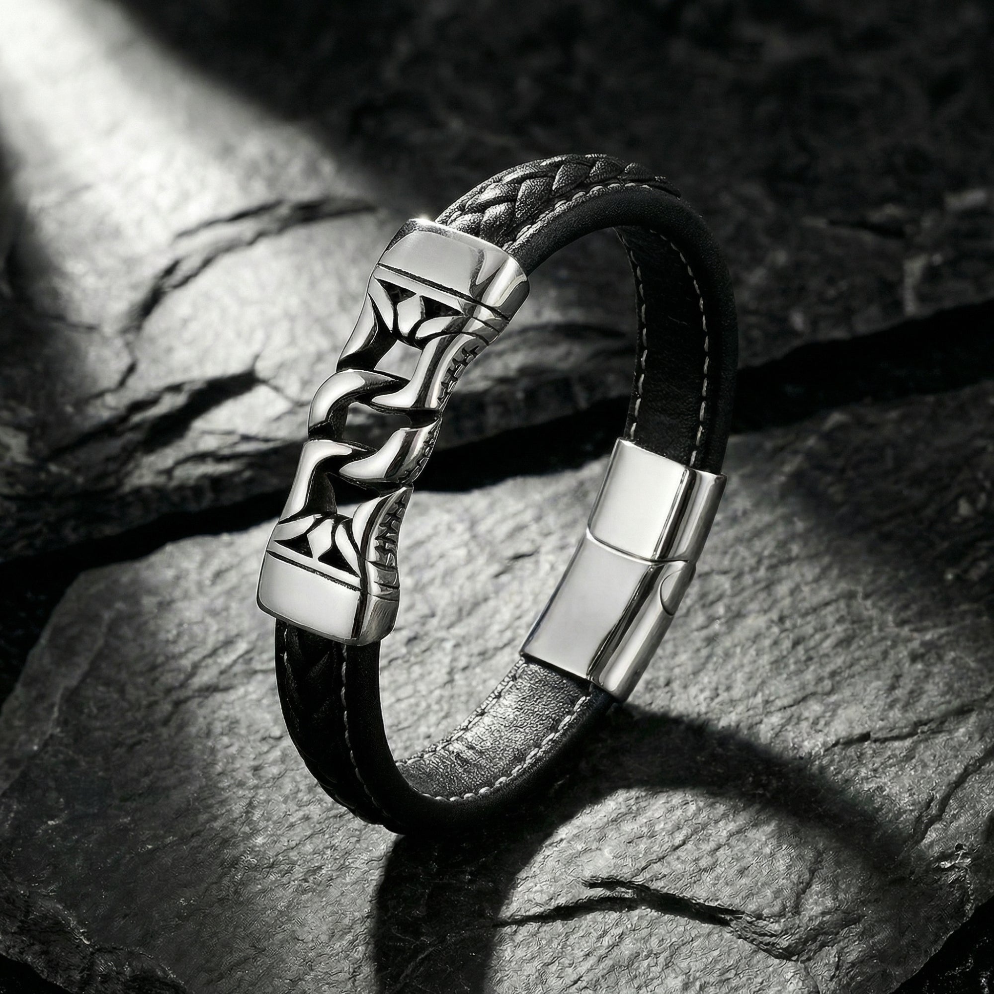 Angled view of the black leather Nexus Bracelet with a silver stainless steel magnetic clasp on a dark rock surface.