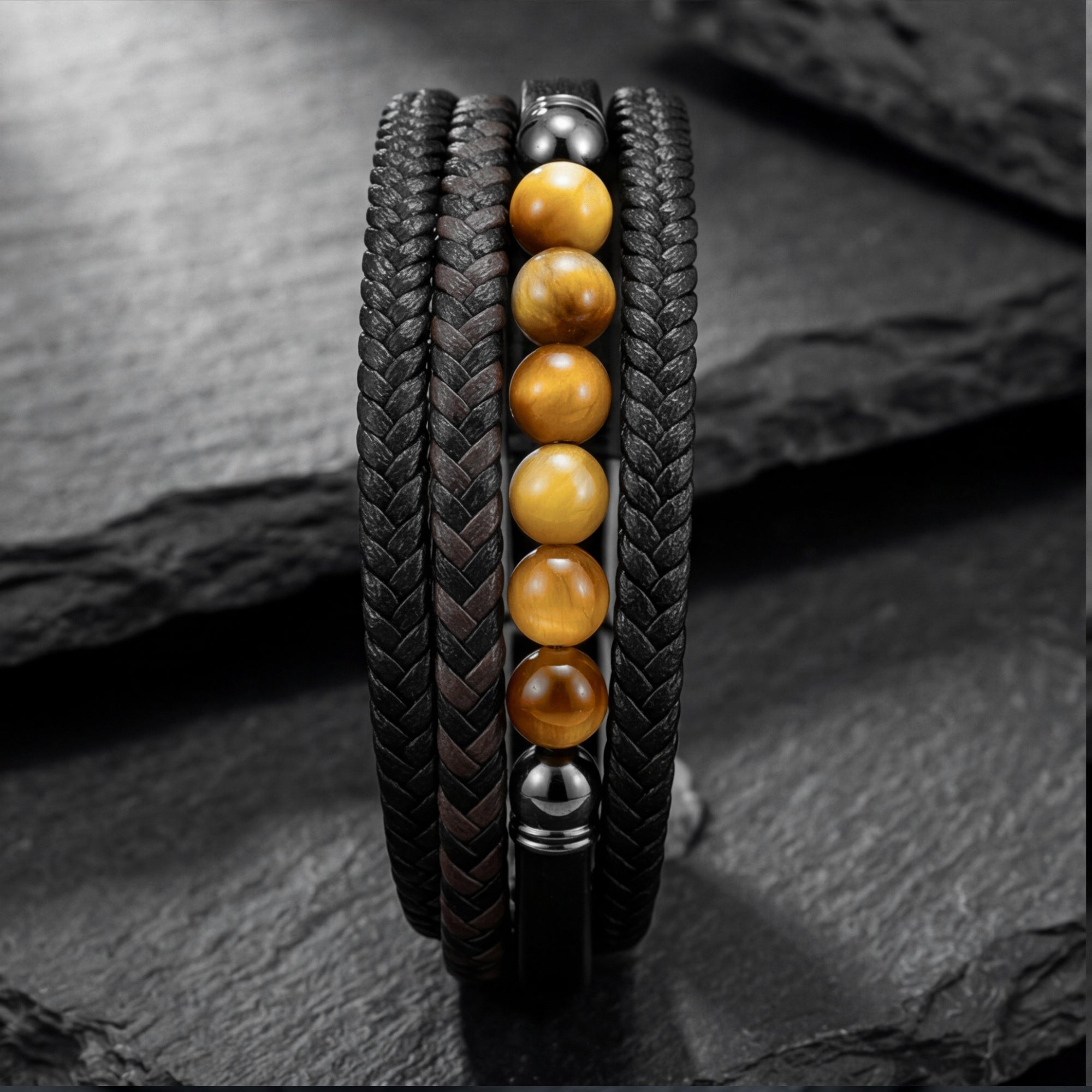 Detail of round yellow tiger eye beads and black braided leather strands on a stainless steel men's bracelet.