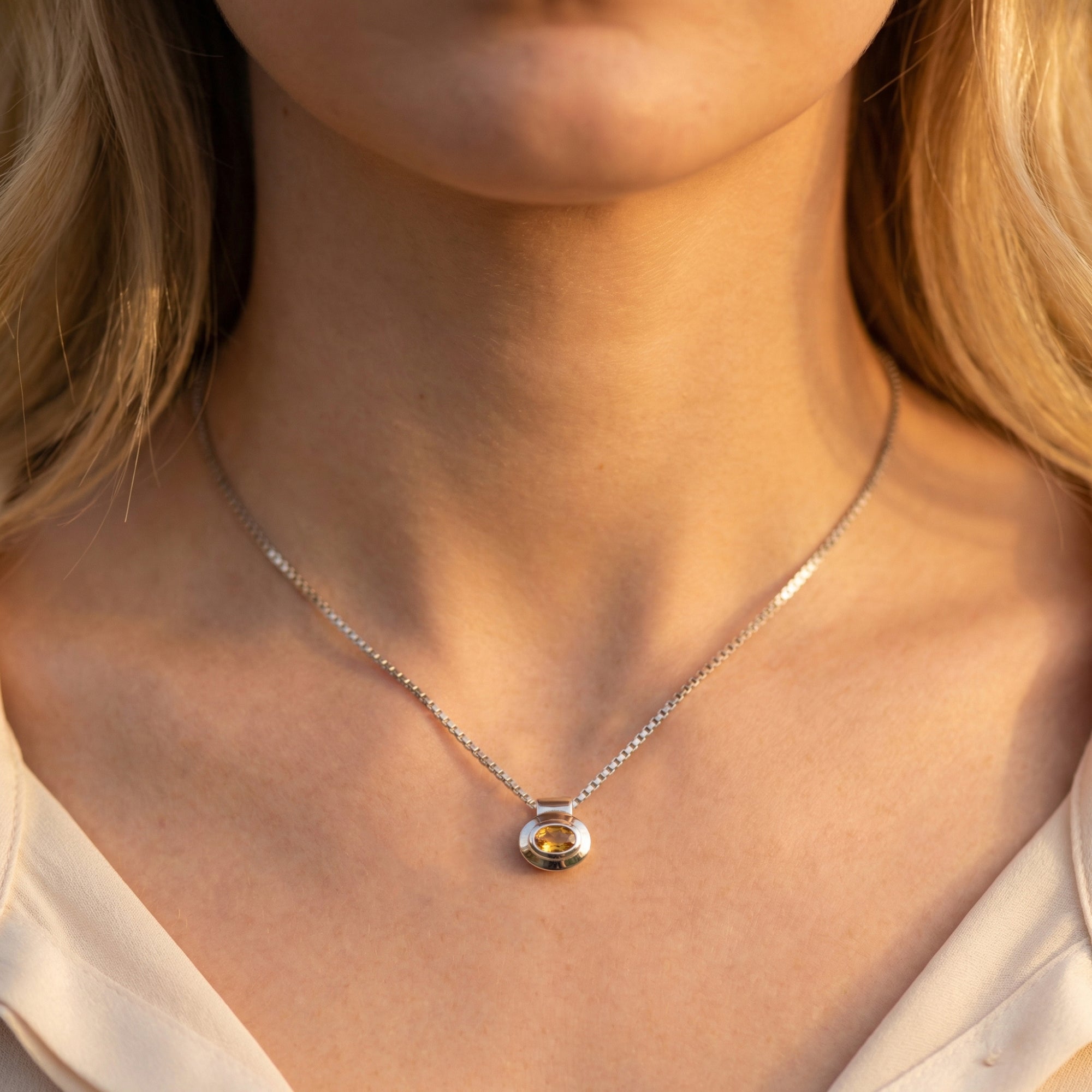 Front view of the Aelia natural citrine necklace in silver worn by a model against a warm, sunlit background.