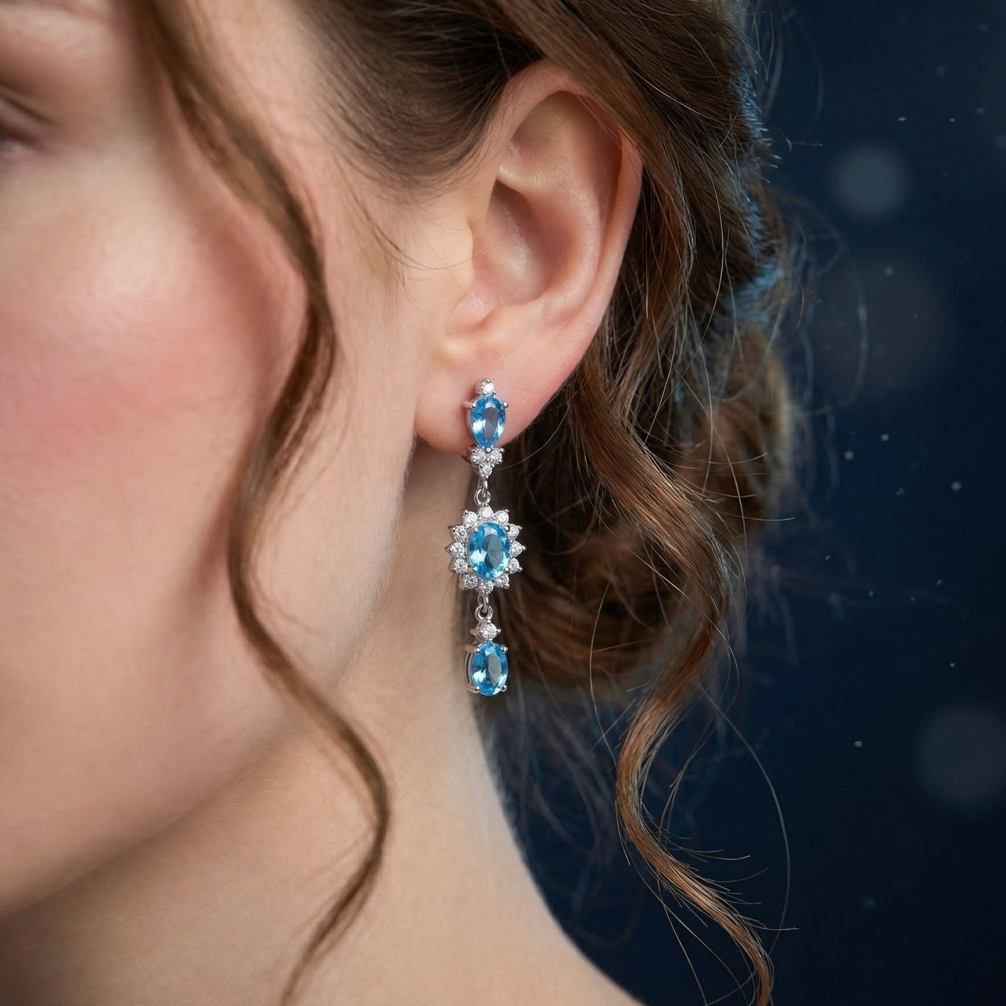 Side view of a model wearing the Ondaria silver drop earrings with vibrant blue topaz and sparkling accents.