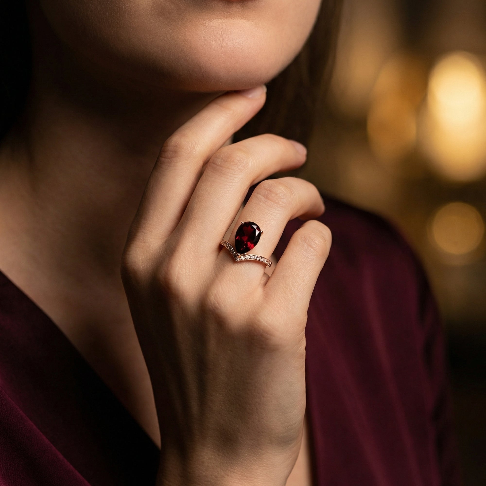 Lifestyle view of a model wearing the pear cut garnet and rose gold chevron ring, paired with a burgundy dress.