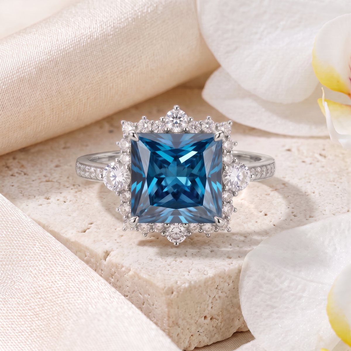 White gold halo ring featuring a square princess-cut blue center gemstone surrounded by brilliant accents.