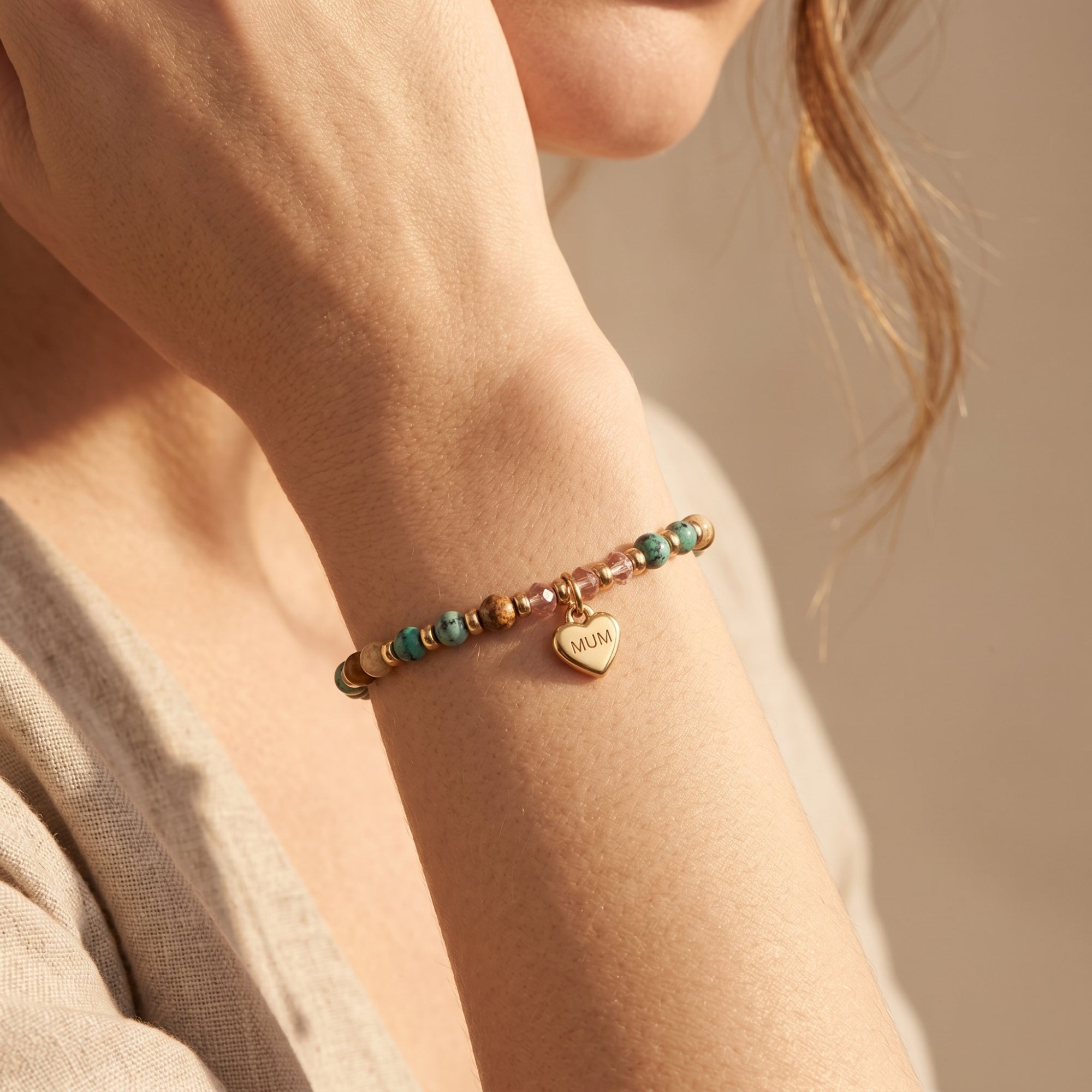 Detail of a gold heart charm bracelet with gemstone beads on a model.