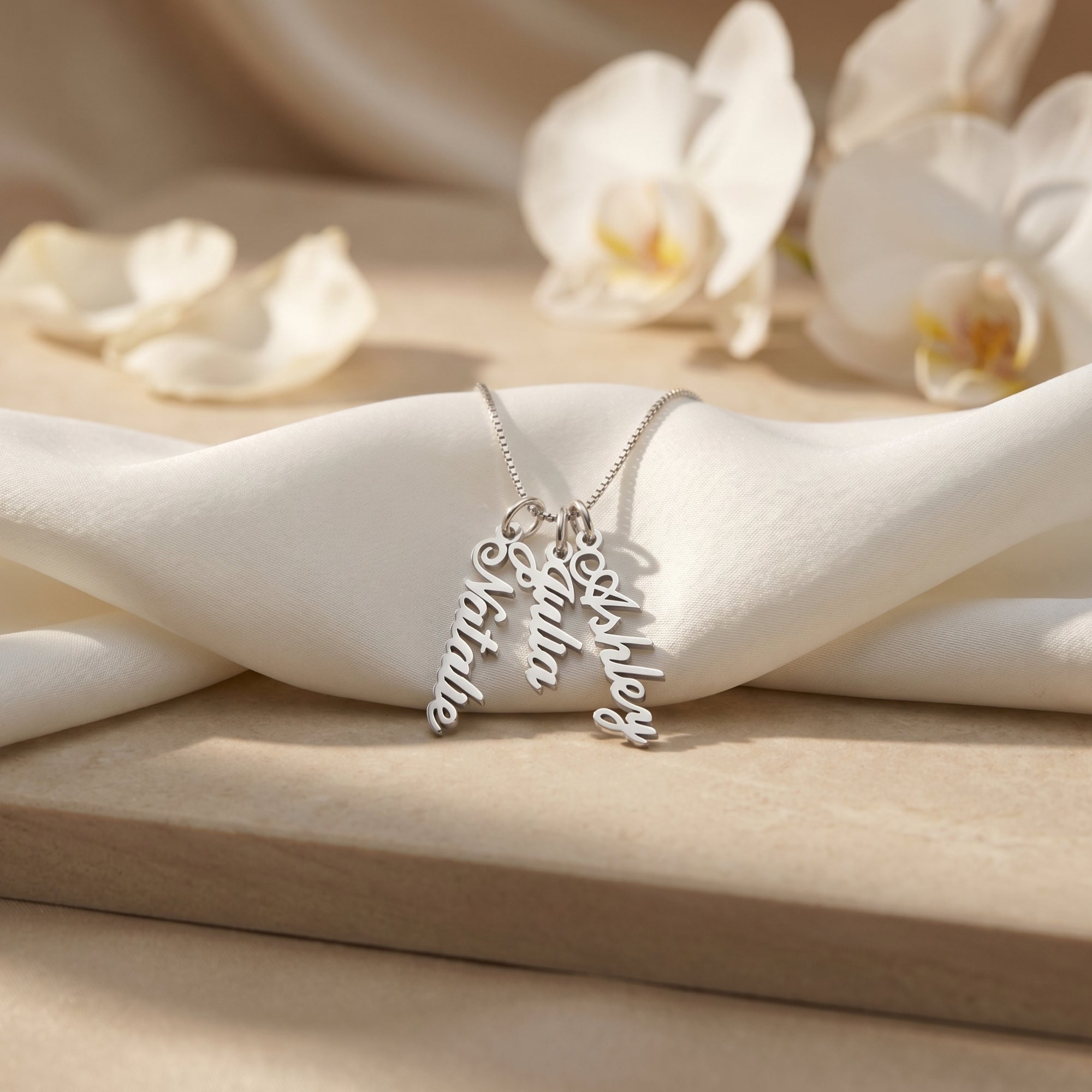 Silver custom name necklace with three vertical pendants on white silk.